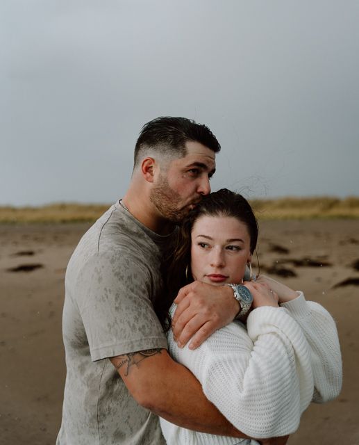 Intimate moment between couple on sandy beach during overcast day.