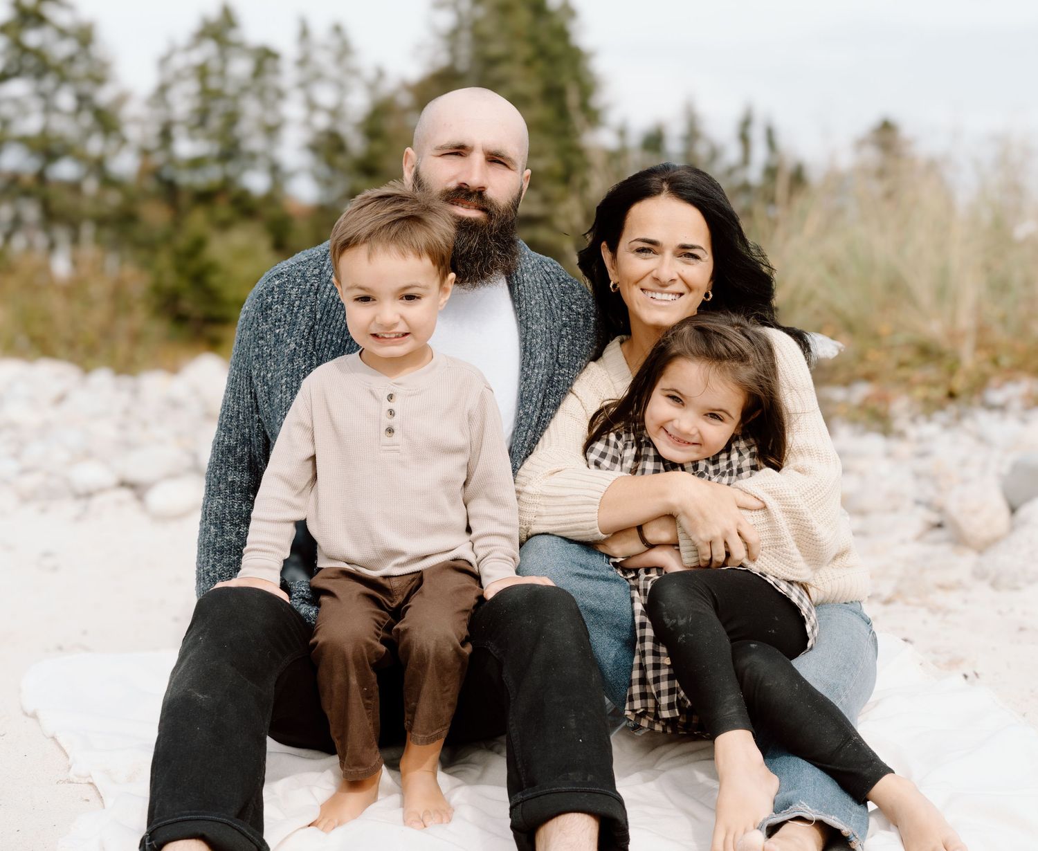 Family sitting together on snowy ground with evergreen trees in background.