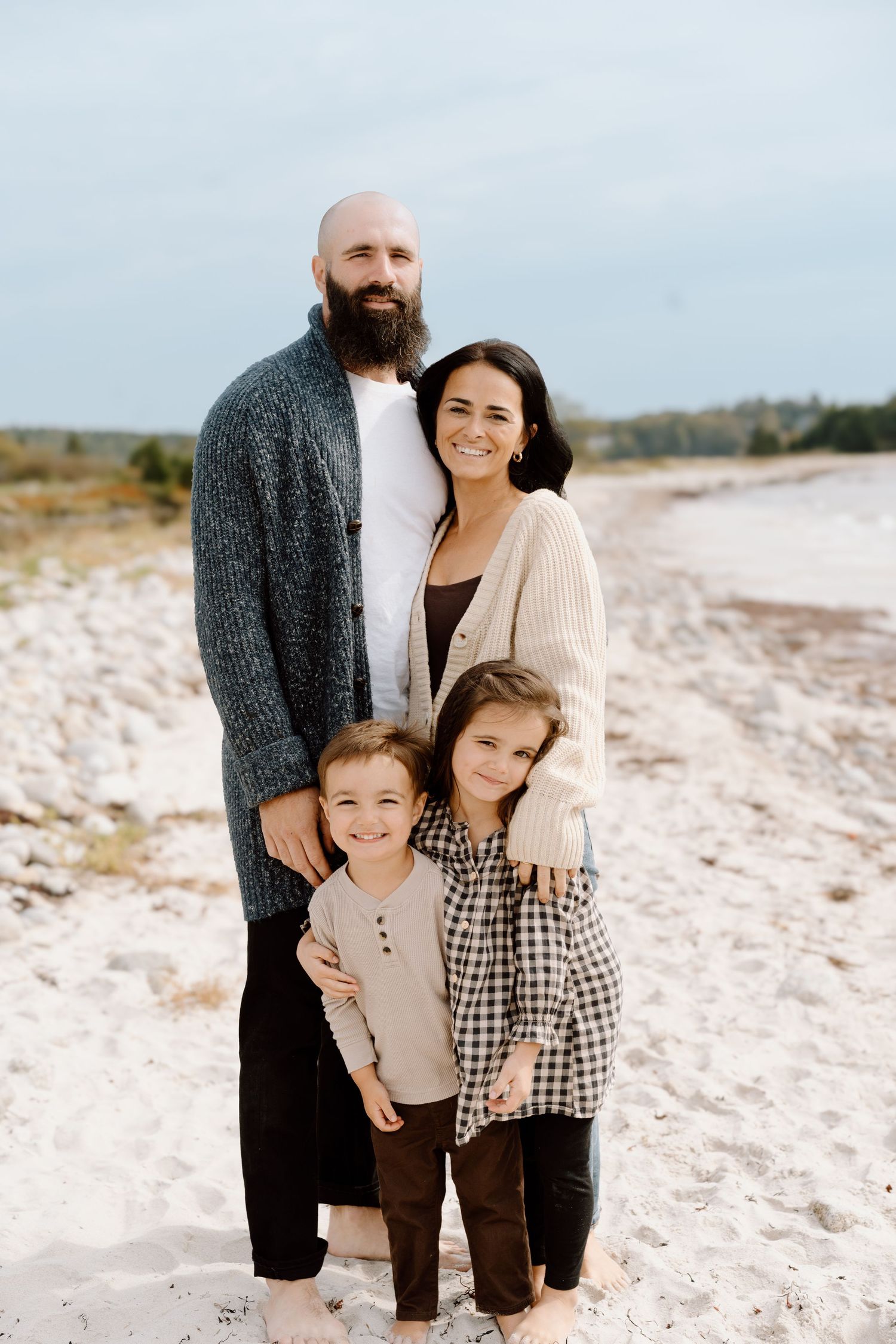Family enjoying a sunny day together at the beach in neutral-colored outfits.