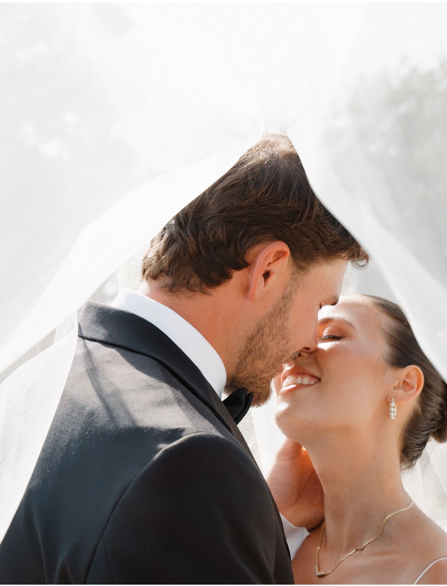 A bride and groom share a romantic kiss under a flowing white veil on their wedding day.