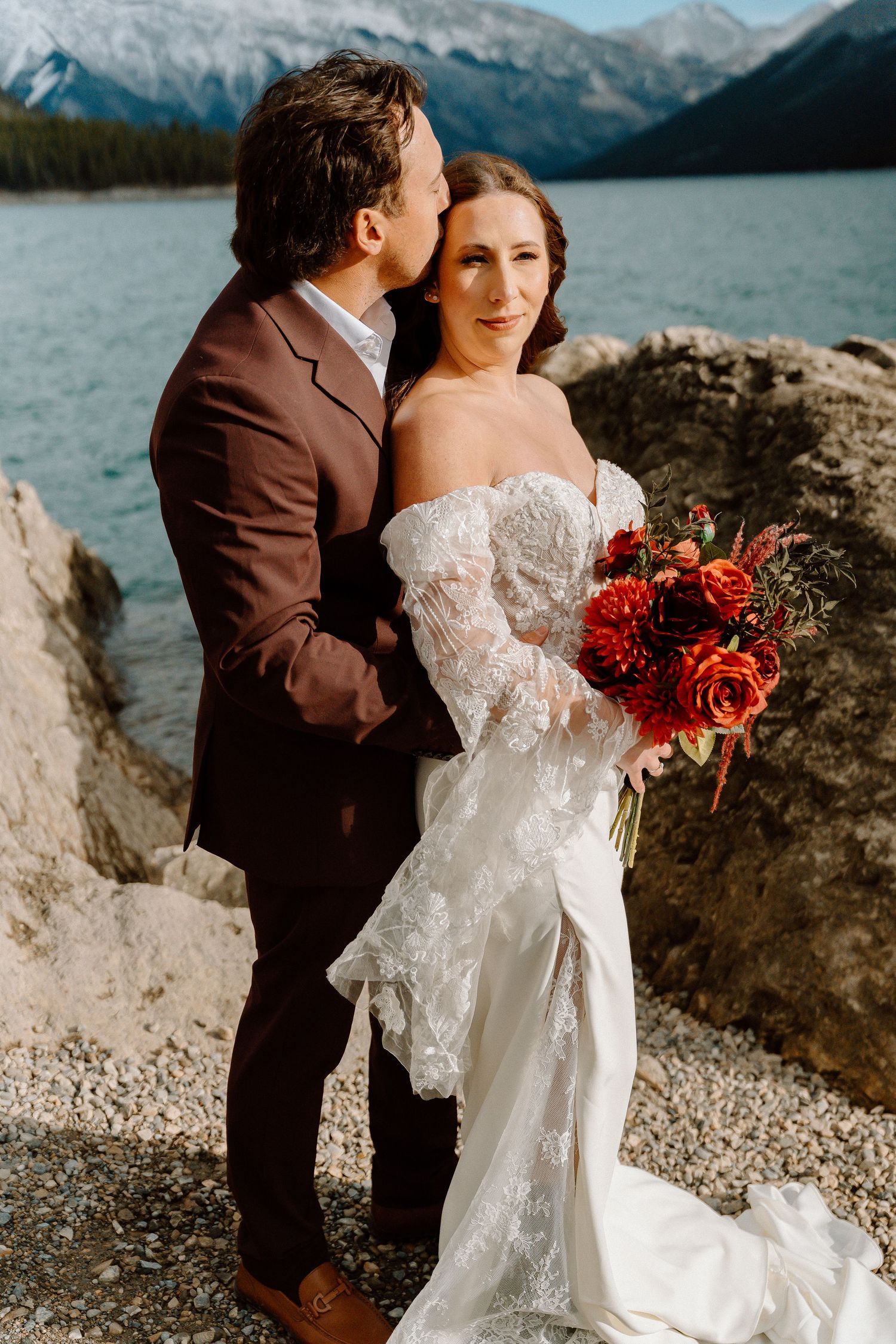 A romantic moment between newlyweds on a rocky lakeshore with majestic mountain peaks in the distance.