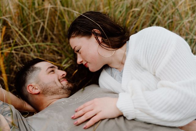 Couple lying in tall grass sharing intimate moment.