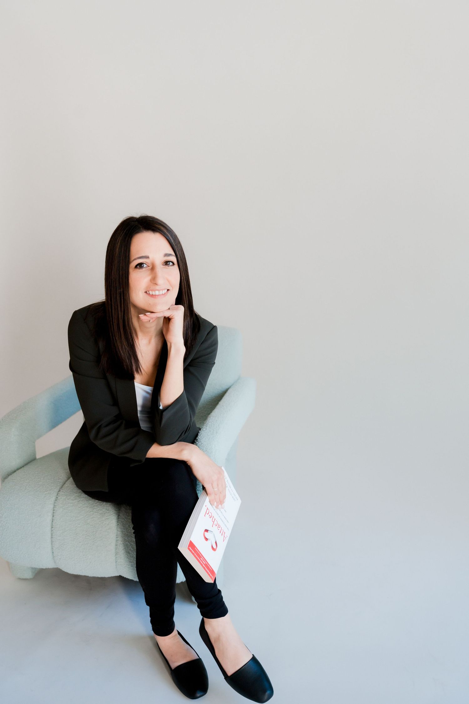 Professional woman in blazer sitting in chair holding documents, smiling confidently.