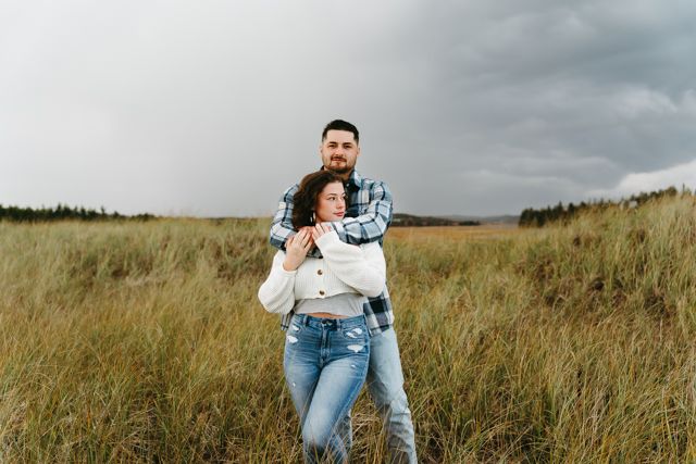Couple walking through a grassy field under cloudy skies.