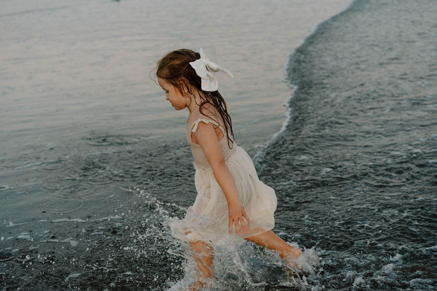 Person in white dress running through shallow ocean water creating dramatic splashes.