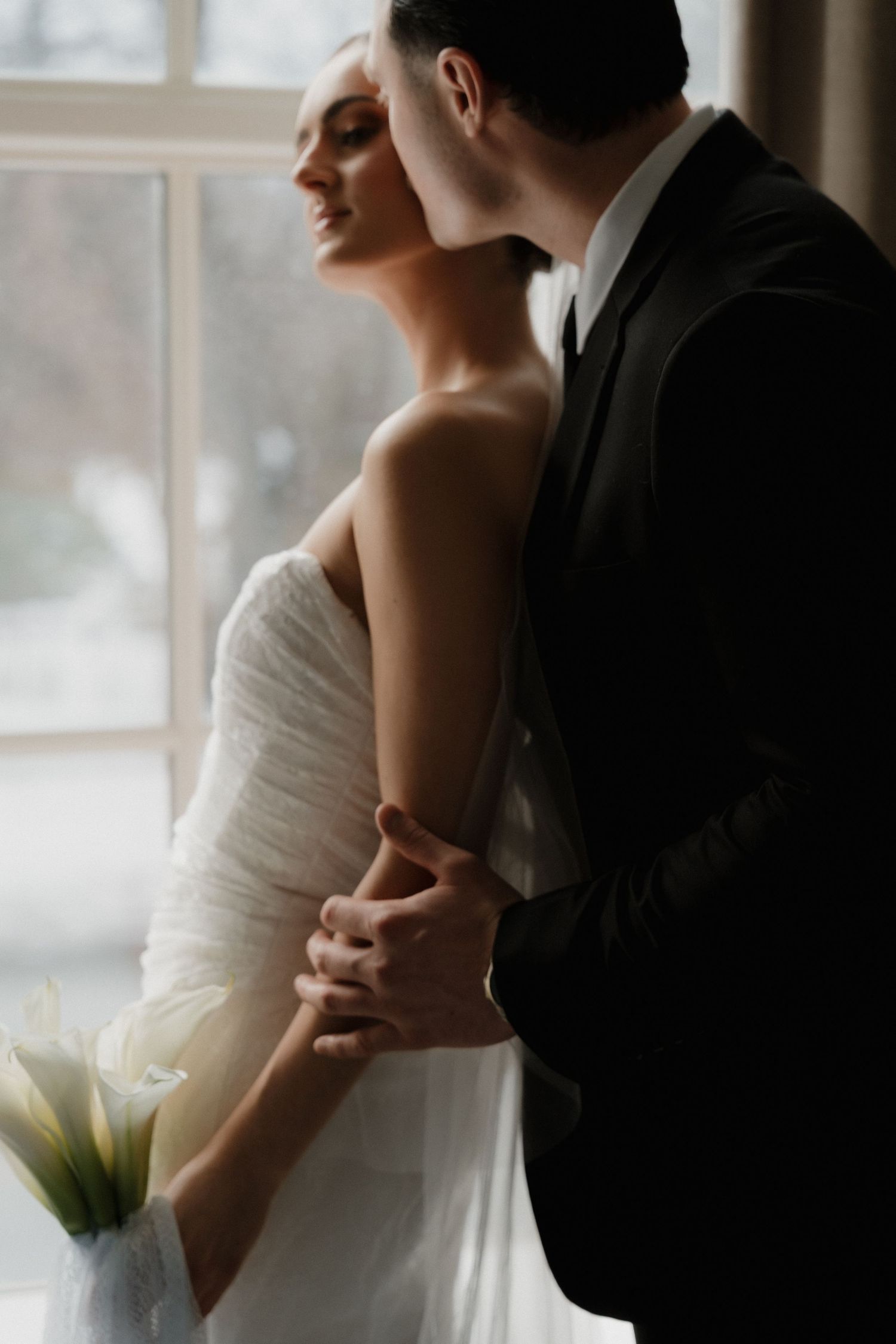 A romantic wedding moment captured in a series of soft-lit photos showing the bride and groom embracing by a window.