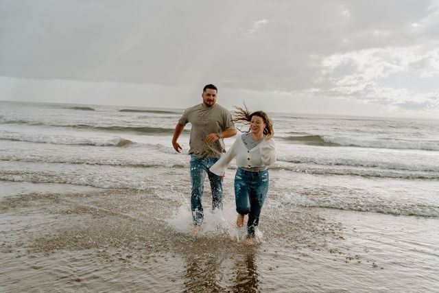 Couple running and splashing together along the beach shoreline.