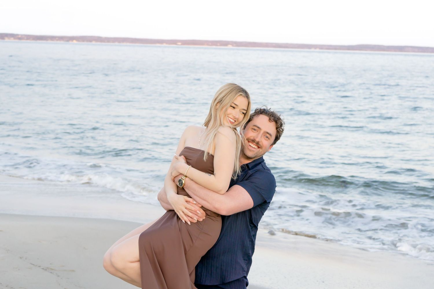 Romantic beach portraits with couple laughing and embracing near ocean waves.