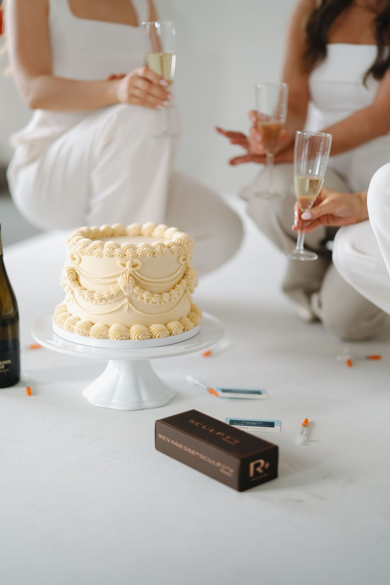 Elegant white cream cake on stand with champagne glasses and chocolate box at a celebration.