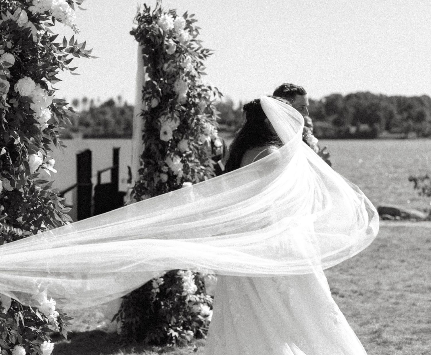 A flowing white wedding veil billows dramatically in the wind across a black and white outdoor scene.