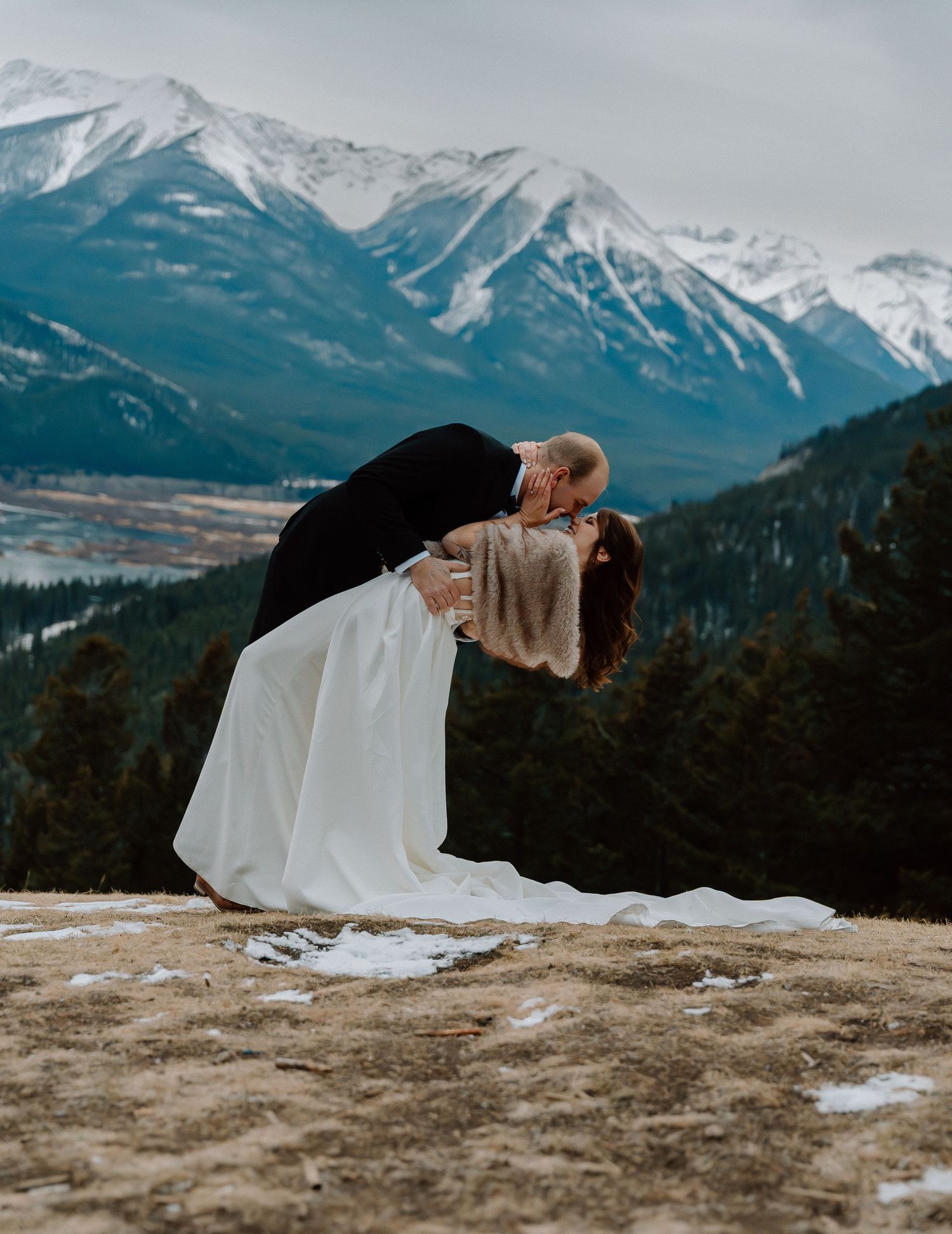 Dramatic wedding dip pose against snowy mountain landscape backdrop.