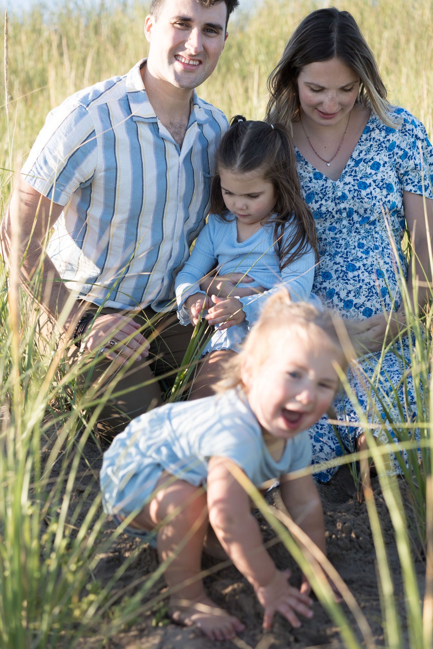 Family playing together in tall grass field during golden hour.