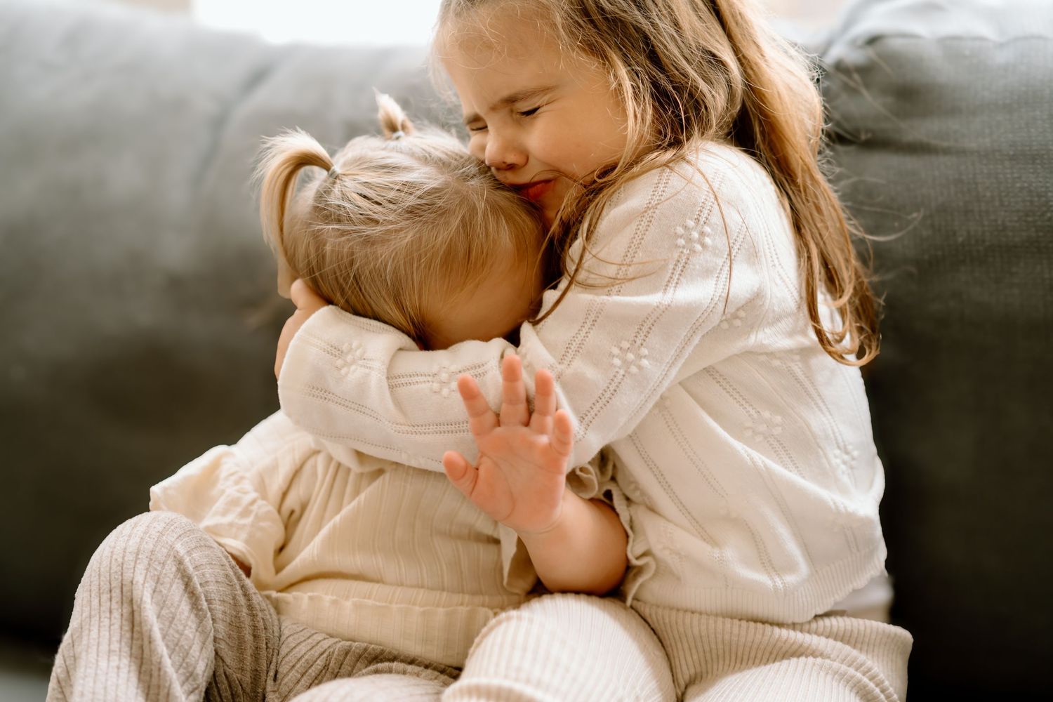 Intimate family cuddle session captured in soft neutral tones on a comfortable bed.