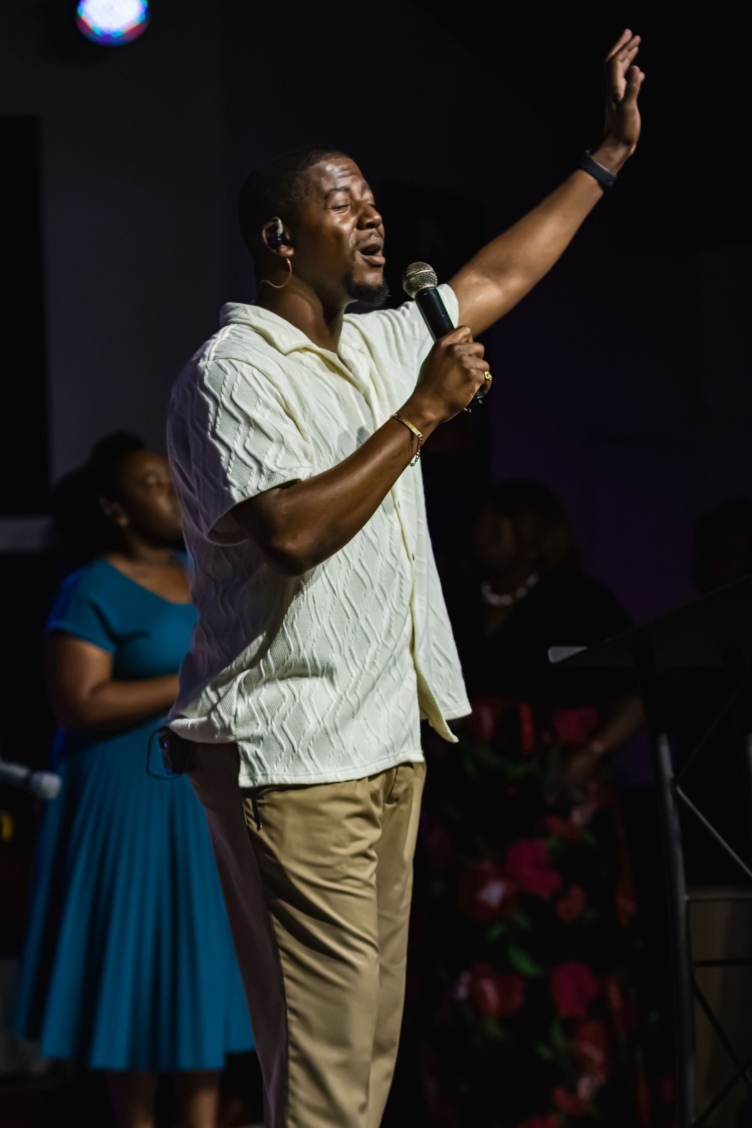 A man sings passionately into a microphone with one hand raised on a dimly lit stage during a live performance.