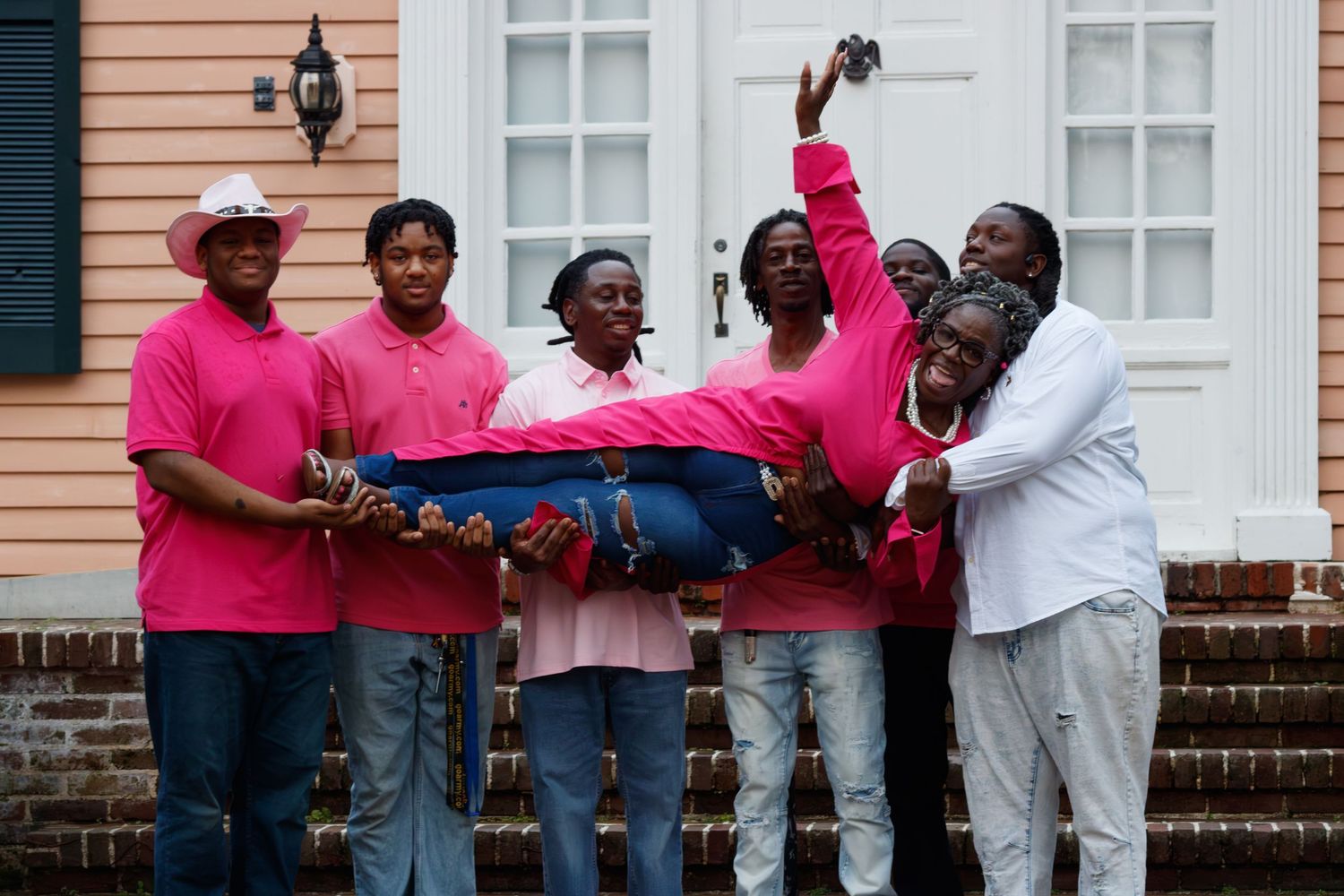 A joyful family in matching pink outfits celebrates together on the steps of a historic building.