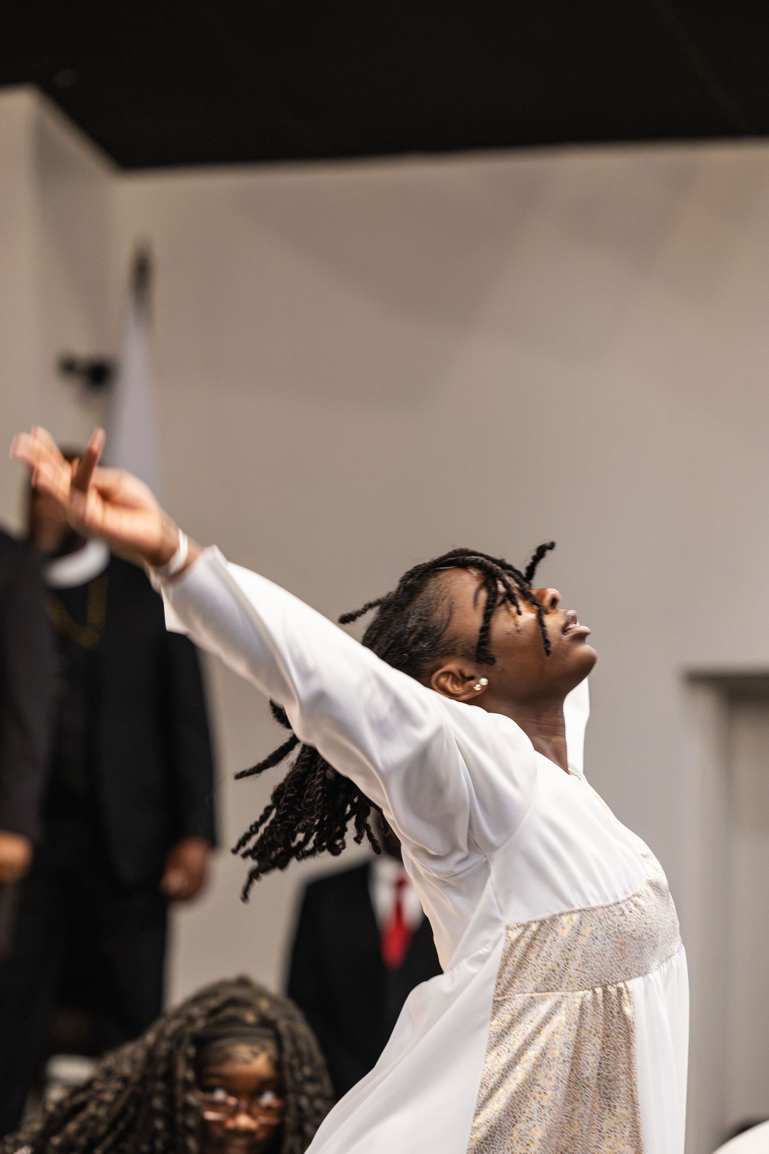 Young woman in white dress performing expressive worship dance with arms raised toward the sky.