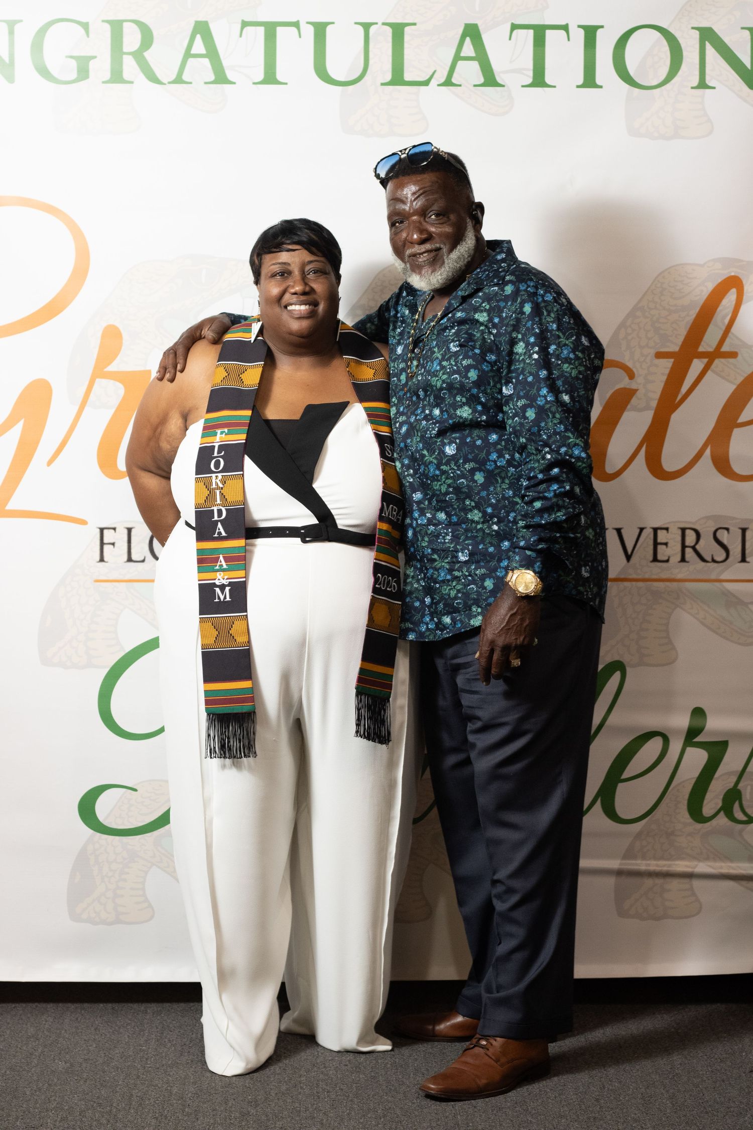 A graduate wearing a Fordham kente stole smiles with an older man at a celebration.