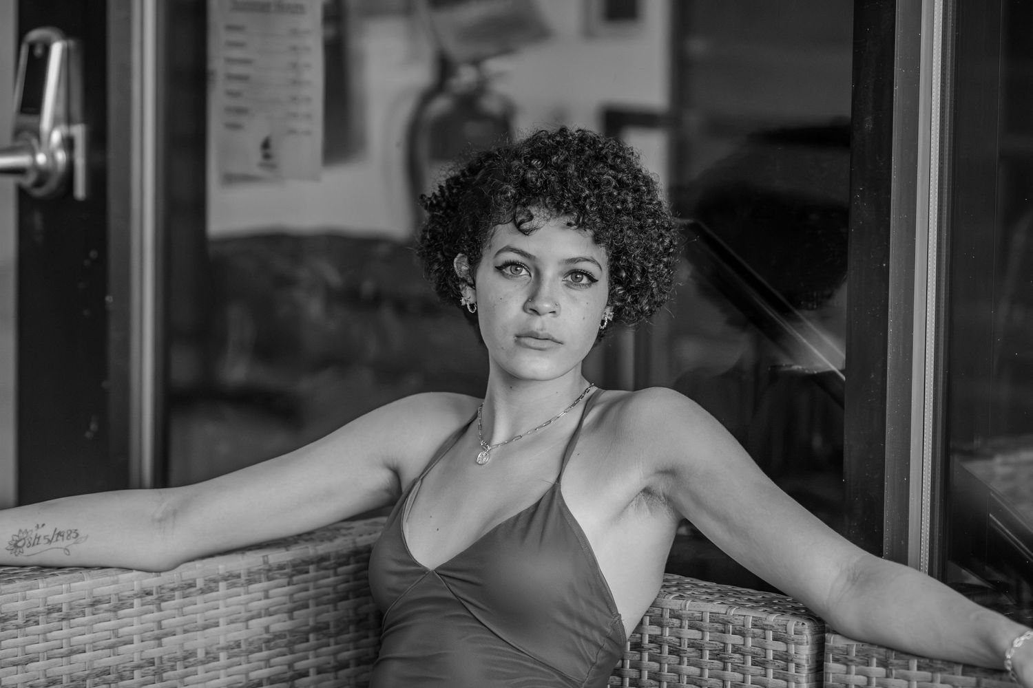 A young woman with curly hair poses thoughtfully at an outdoor cafe in a black and white portrait.