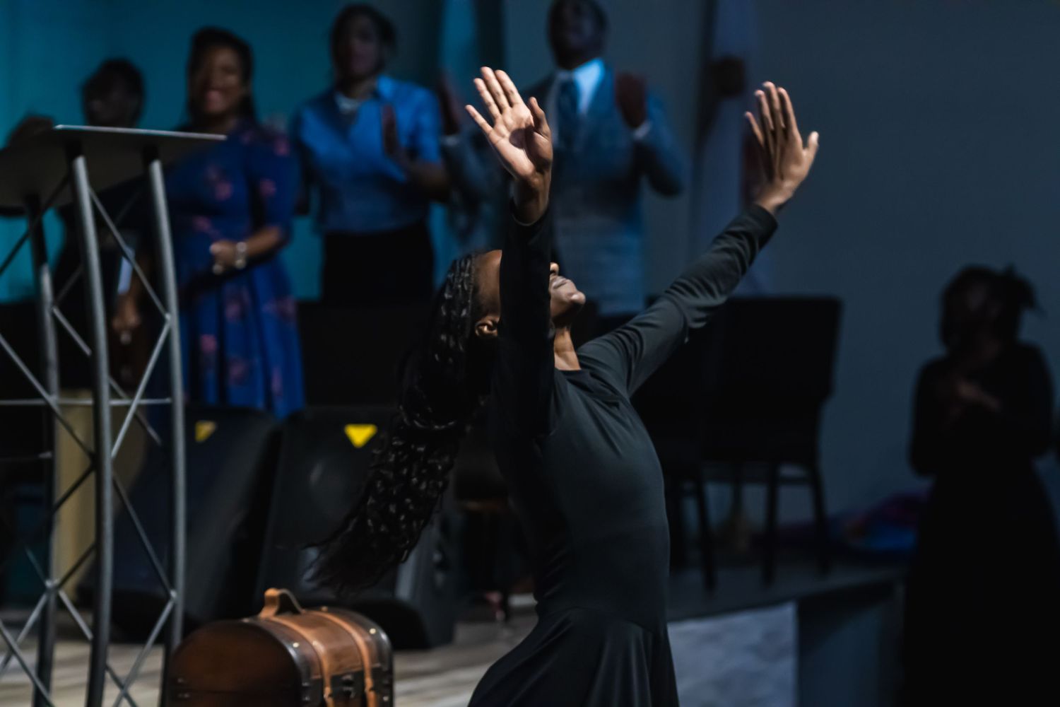 A woman in black performs an expressive worship dance with arms raised during a church service.