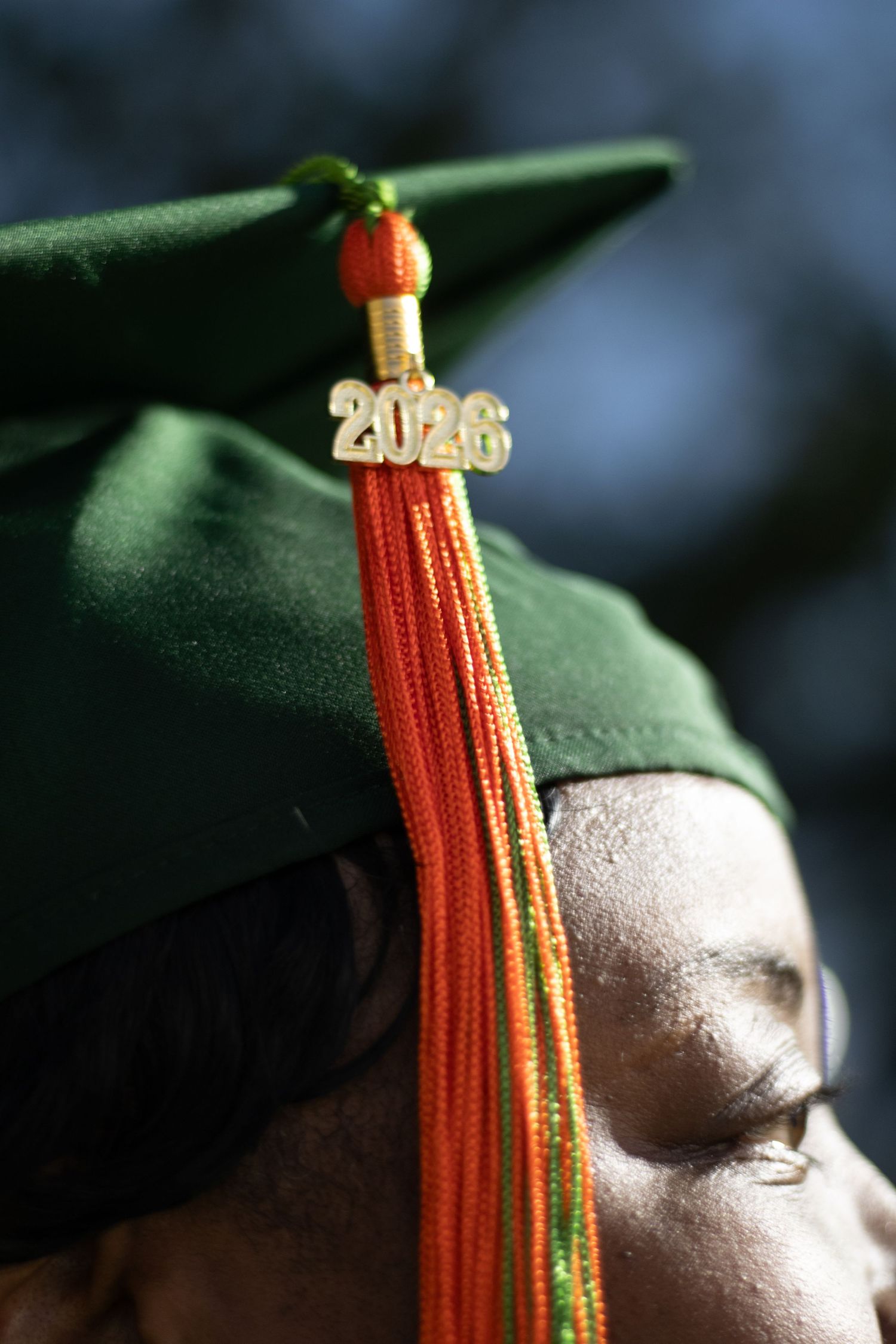 Close-up of a green 2026 graduation cap with orange tassel on a graduate's head.