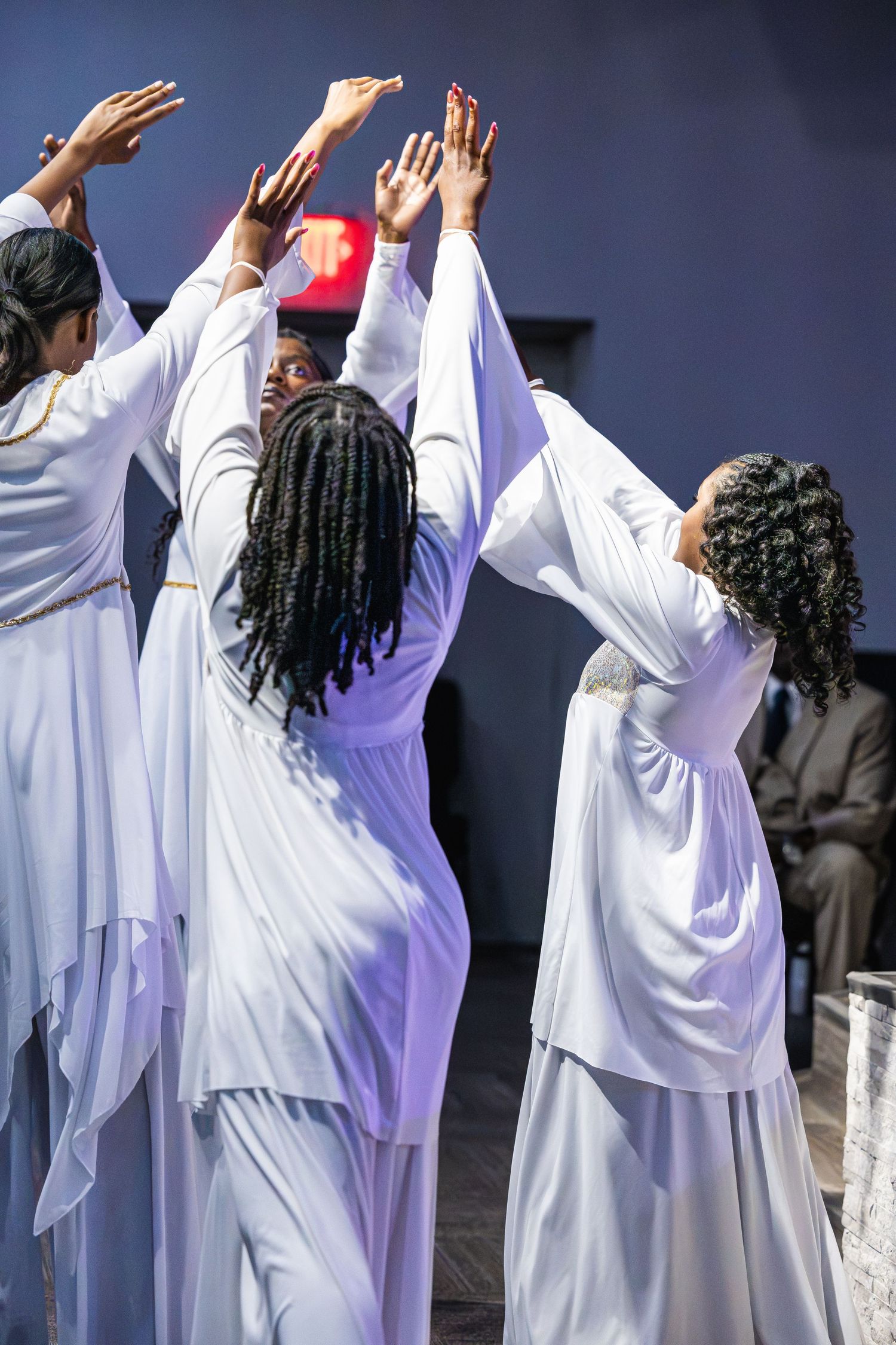 Group of women in white robes performing a praise dance with arms raised in a church setting.