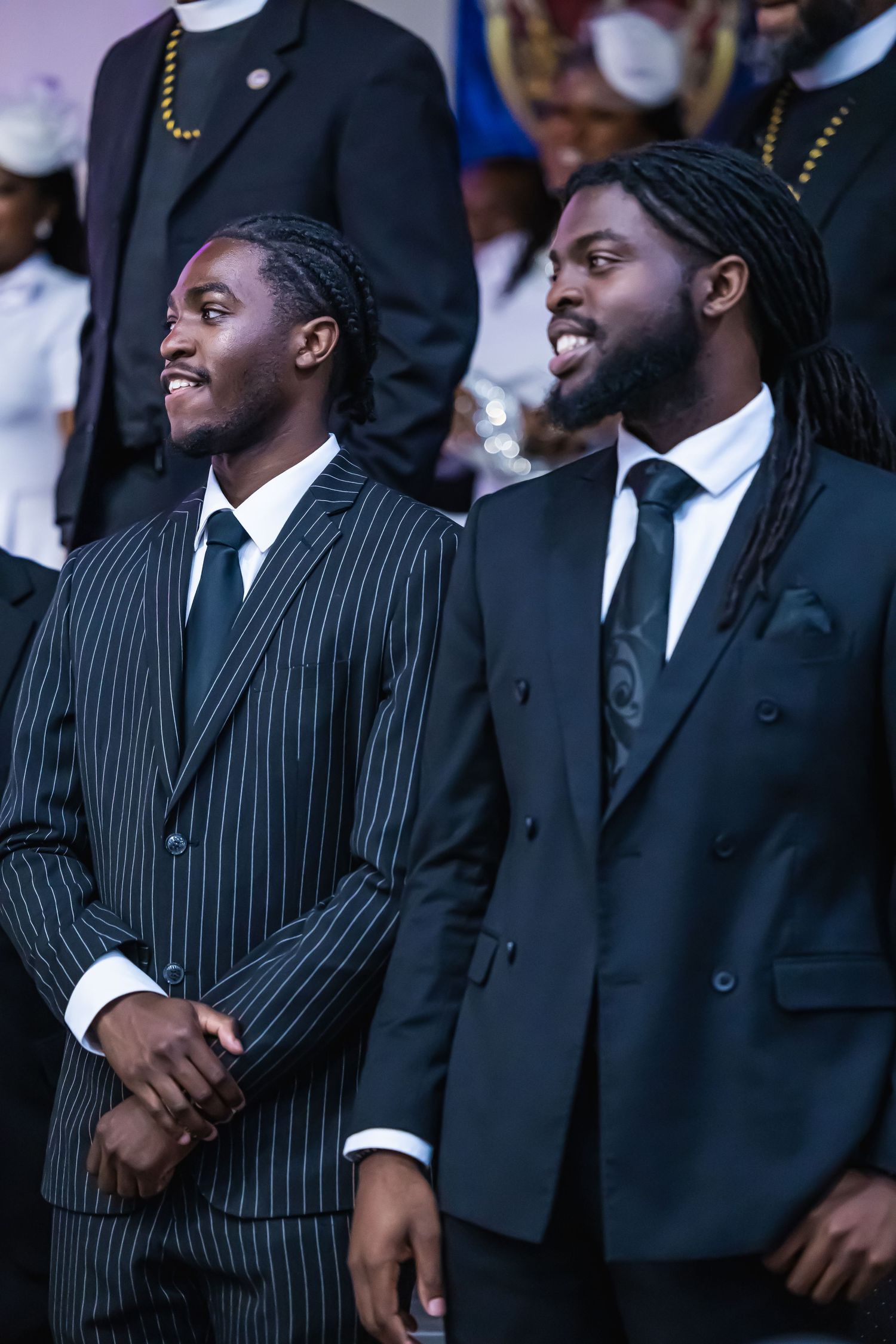 Two well-dressed young Black men in dark suits and ties smiling at a formal event.