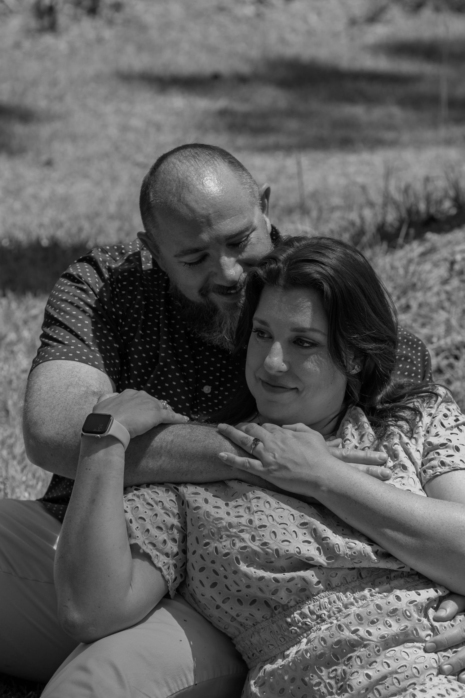 A black and white photo of a couple relaxing together outdoors in a tender embrace.