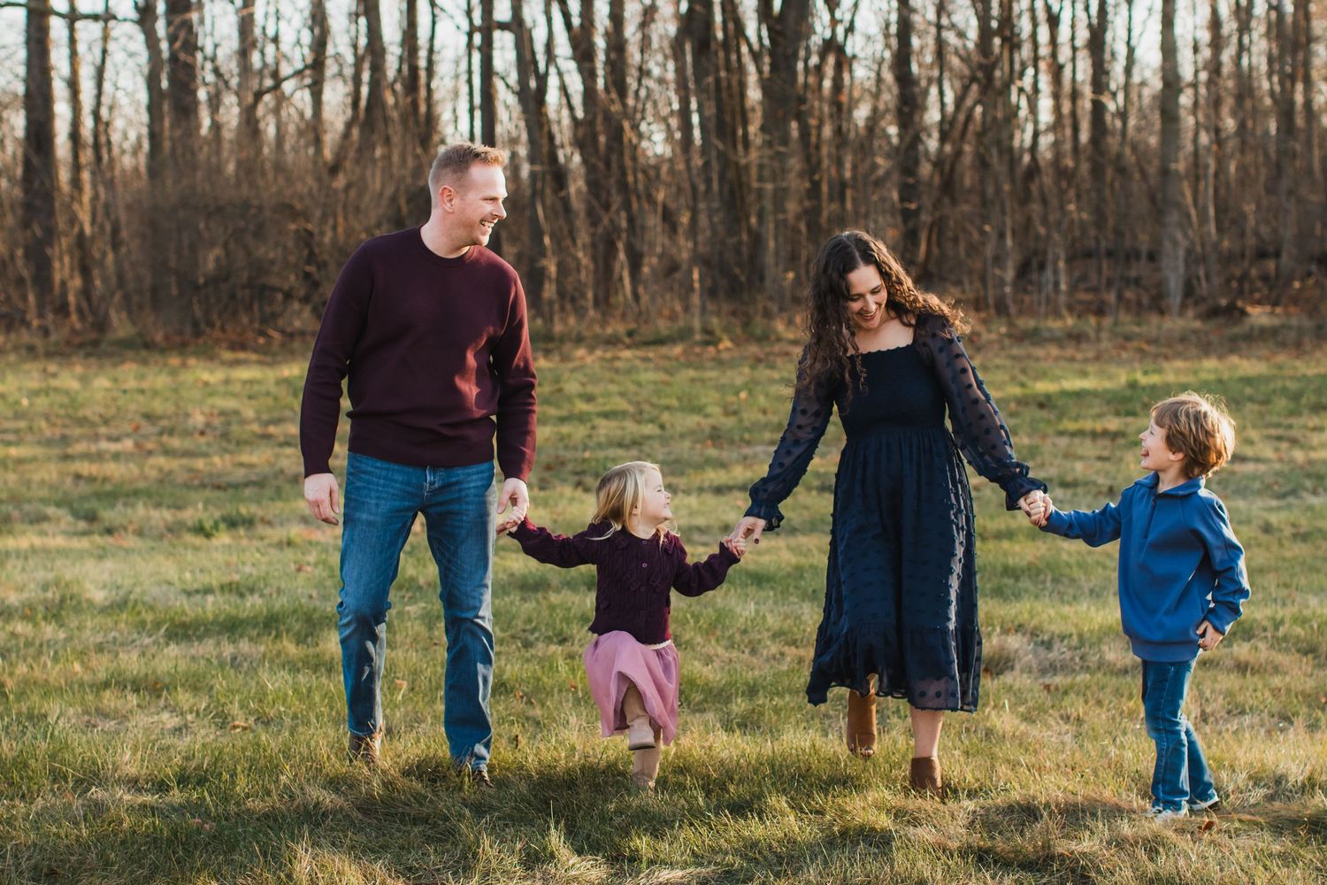 Happy family of four holding hands and walking together in an autumn outdoor field.