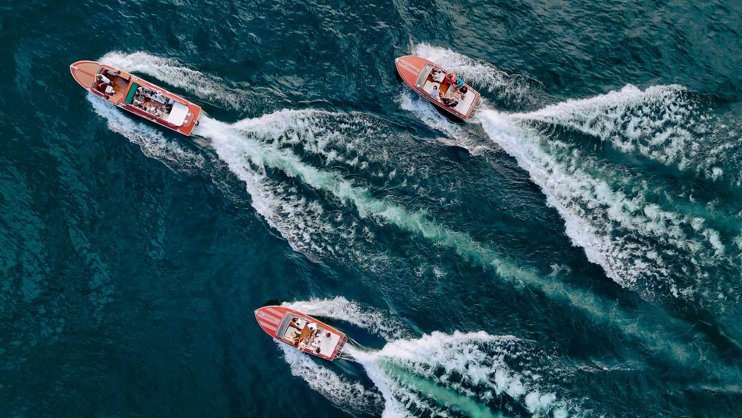 Aerial view of three red speedboats racing through deep blue waters in Lake Como