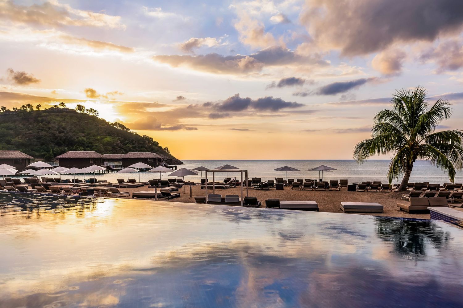 Stunning sunset over a tropical resort infinity pool with palm trees and ocean views.