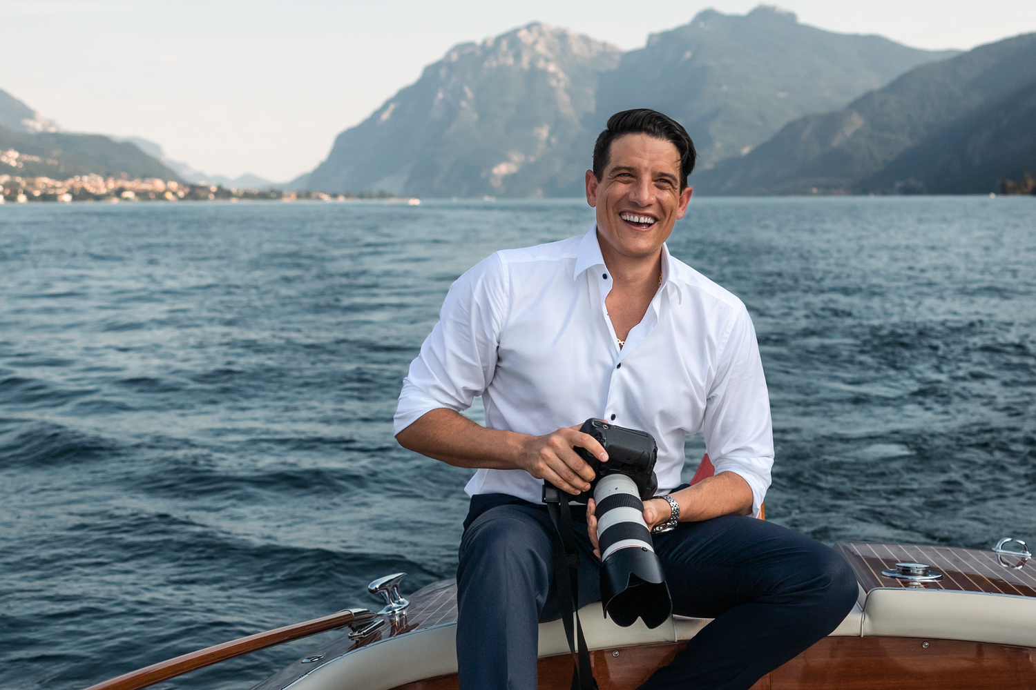 Giuseppe DeMasi on a boat in Lake Como, Italy with camera equipment against a mountain lake backdrop.