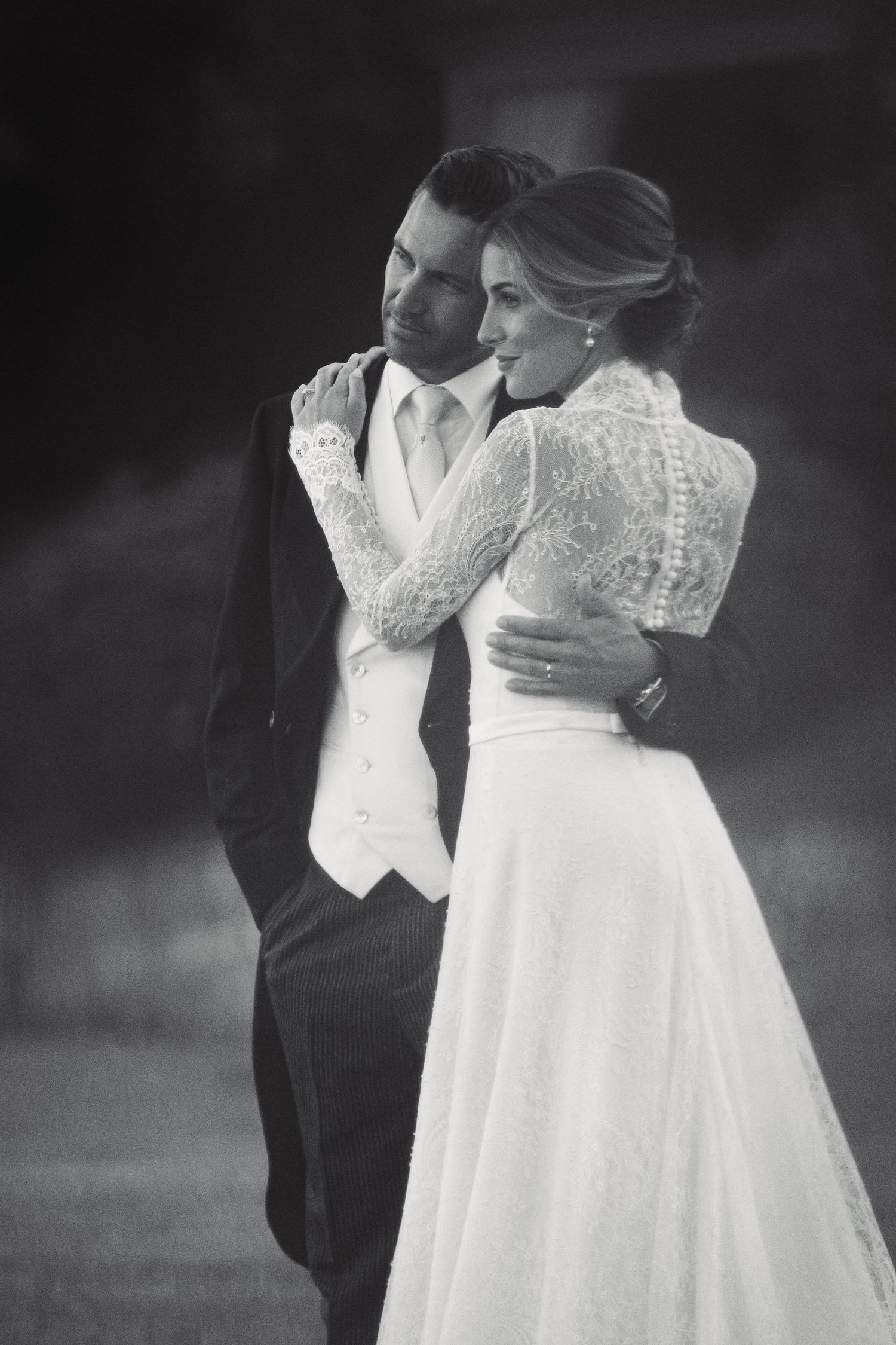 A romantic black and white wedding portrait captures a tender embrace between newlyweds in traditional formal attire.