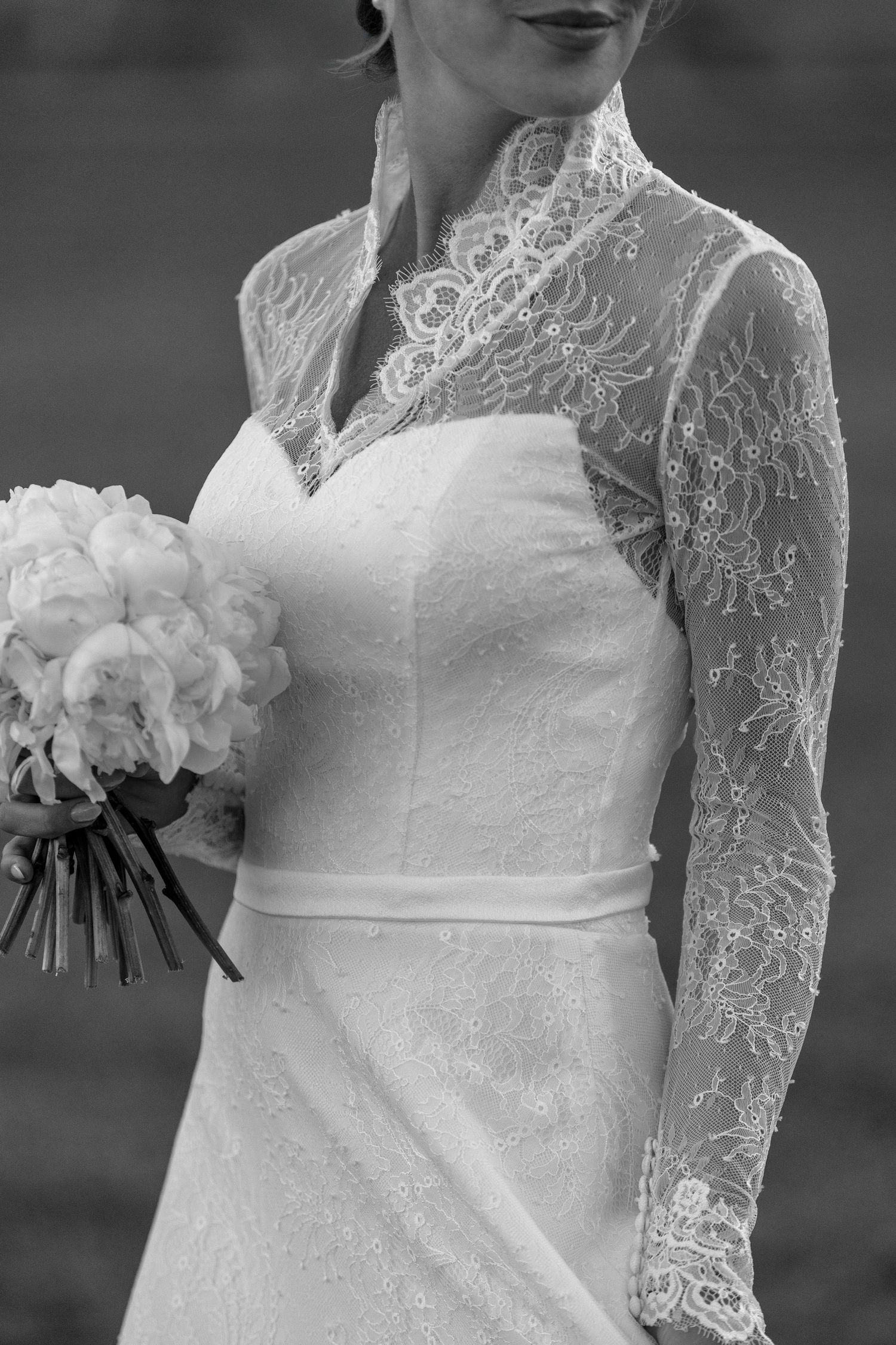 Bride in a lace-sleeved gown holding a bouquet in soft, cinematic light.