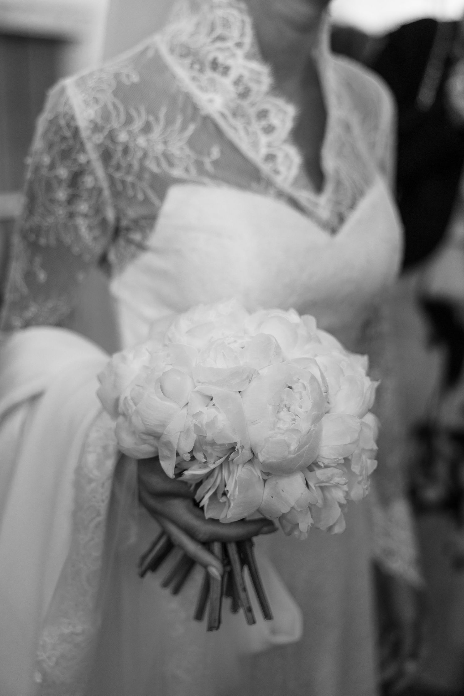 A black and white photo of a delicate white lace wedding dress and bridal bouquet of white peonies.