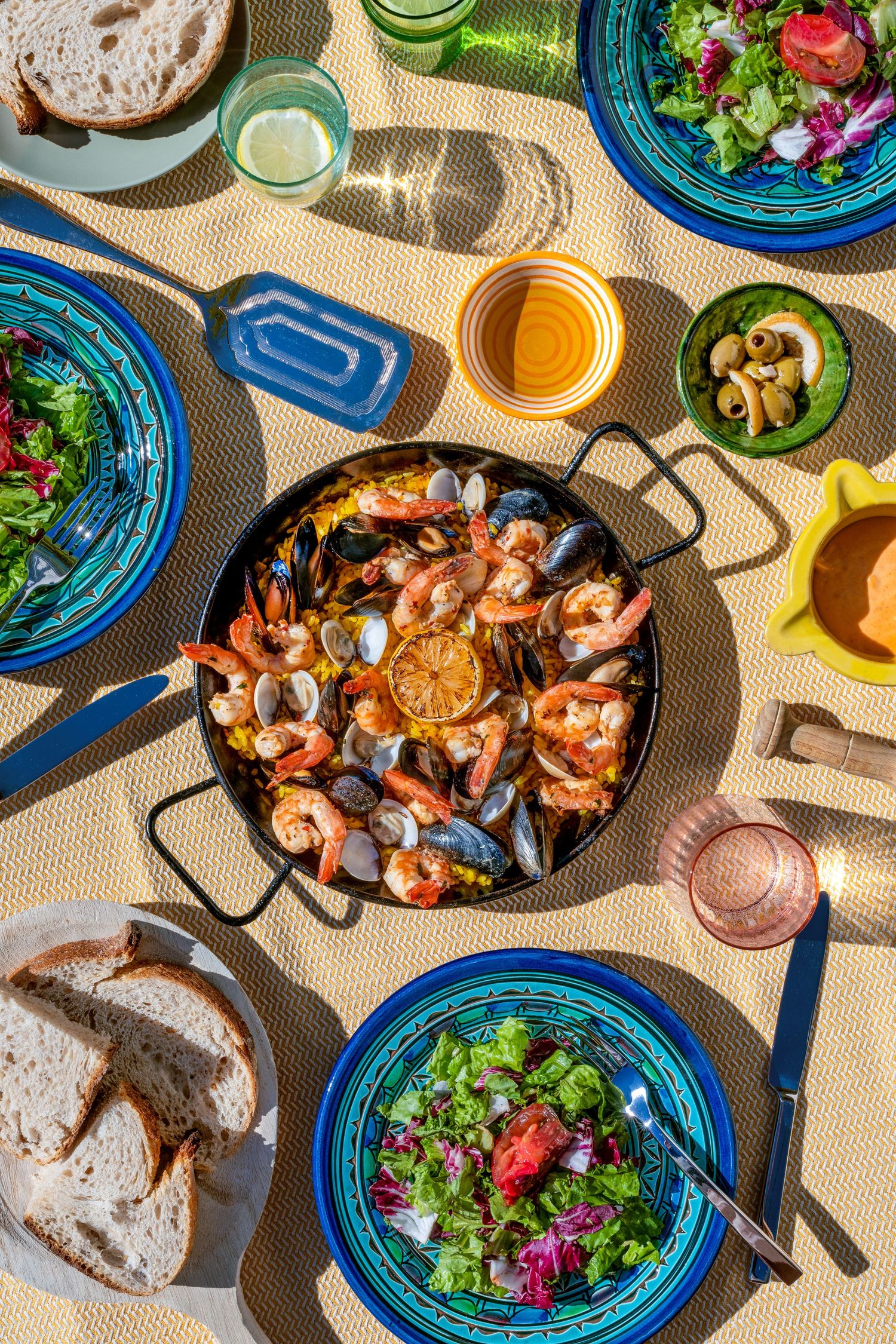 Overhead view of seafood paella with shrimp and mussels served with fresh salads and bread on bright blue plates.