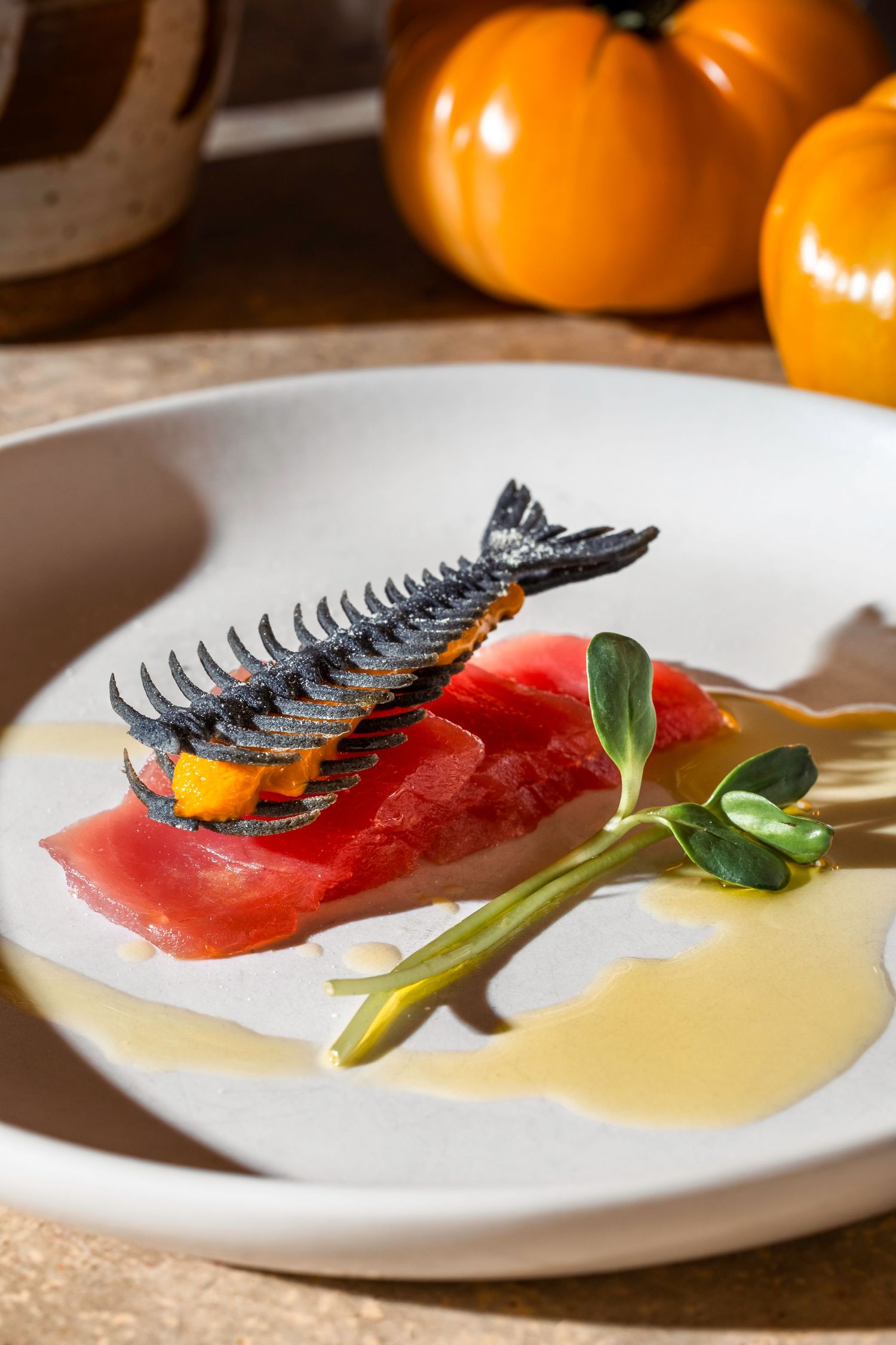 Elegant sashimi dish with fresh tuna topped with crispy fish skeleton and microgreens on a white plate with citrus sauce.