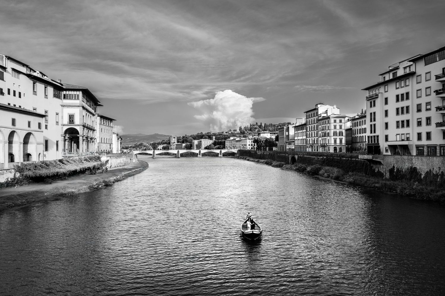 Black and white photograph of a small boat on the Arno River in Florence with historic buildings lining both riverbanks.