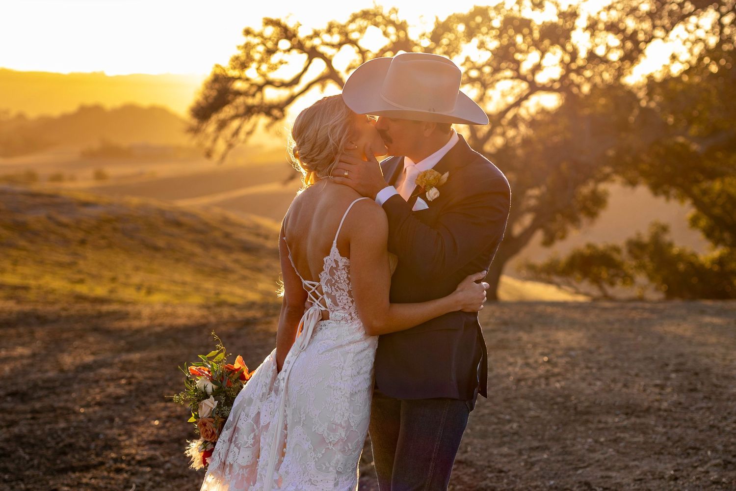 A wedding couple shares an intimate moment at sunset with a golden landscape behind them.