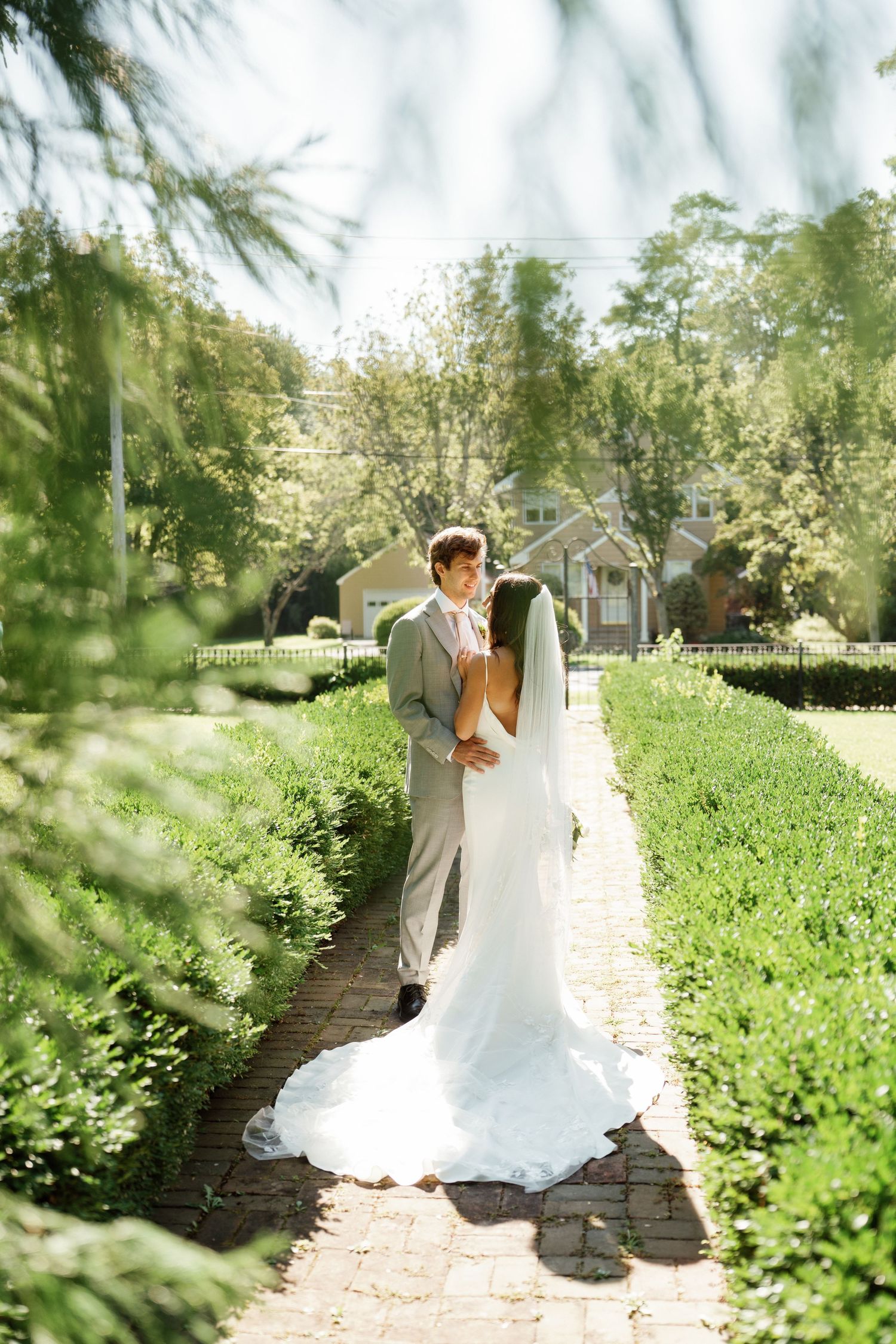 Bride and groom share intimate moments along a garden path surrounded by lush greenery.