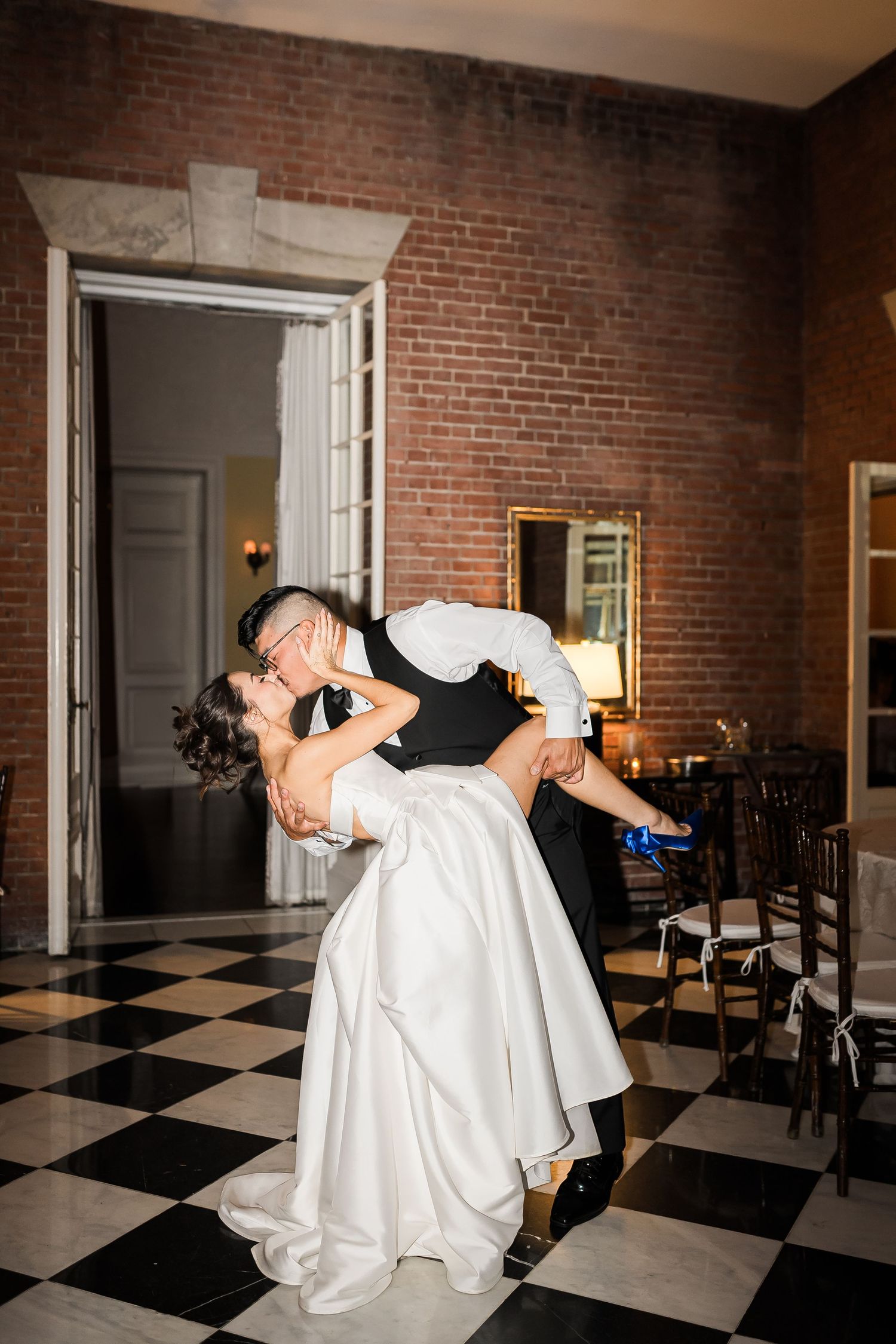 Dancing couple sharing romantic dip on checkered floor with exposed brick walls.