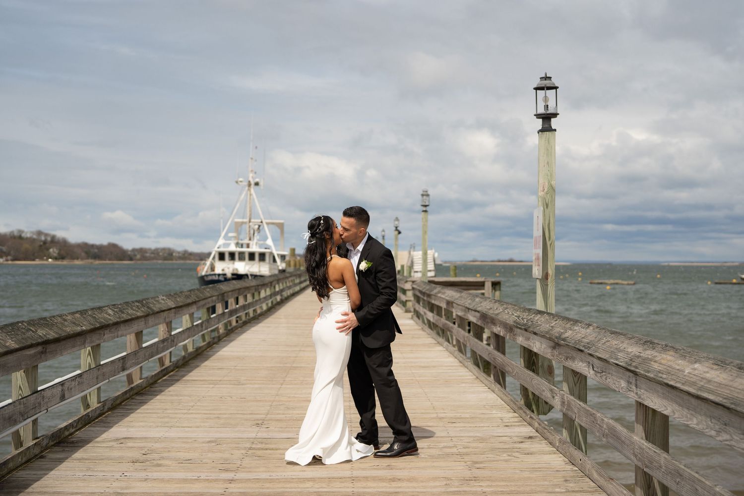 A couple shares a romantic moment on a wooden pier overlooking the ocean under cloudy skies.