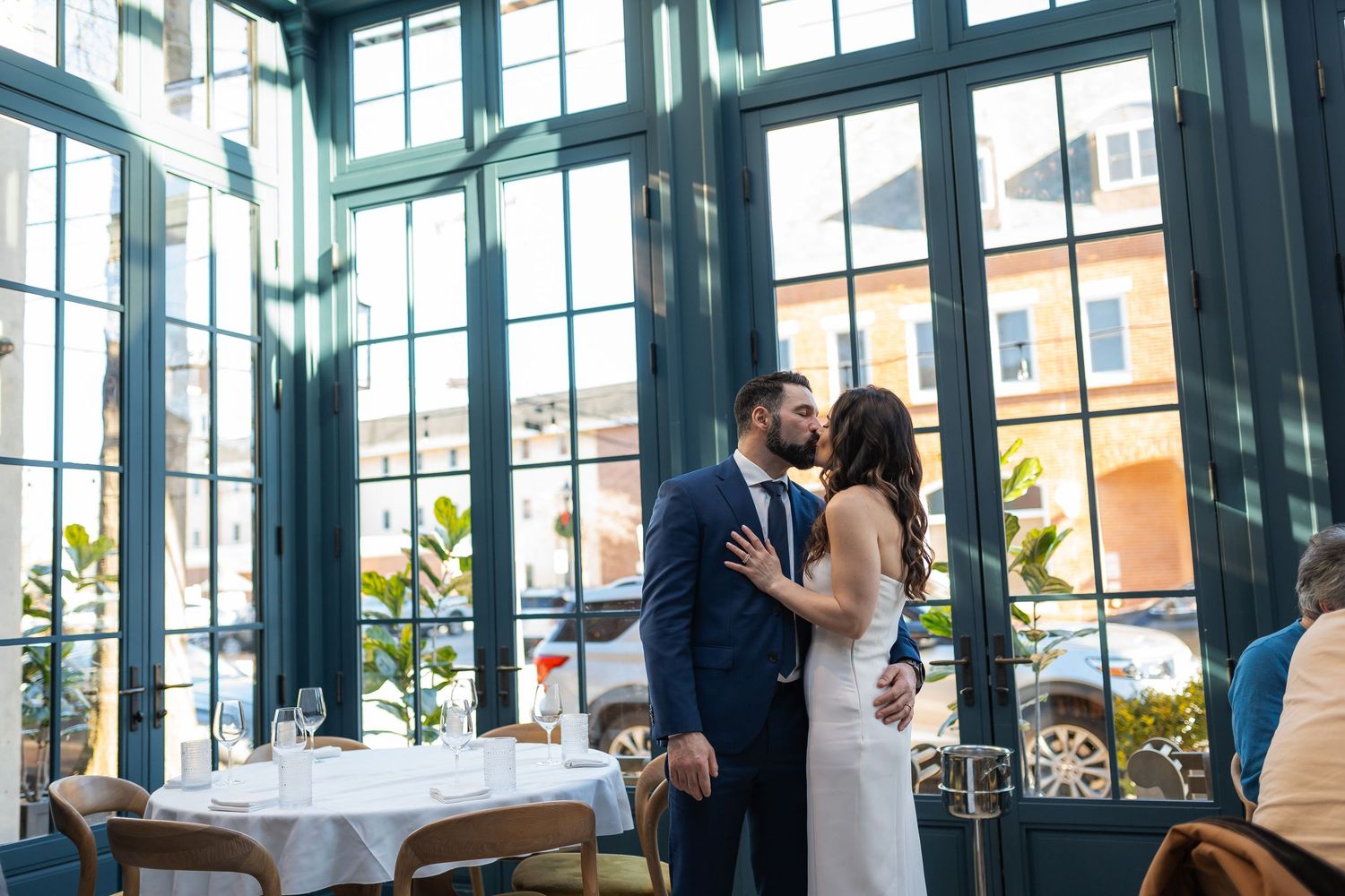 A romantic moment shared between a couple in formal attire inside an elegant glass-walled restaurant.