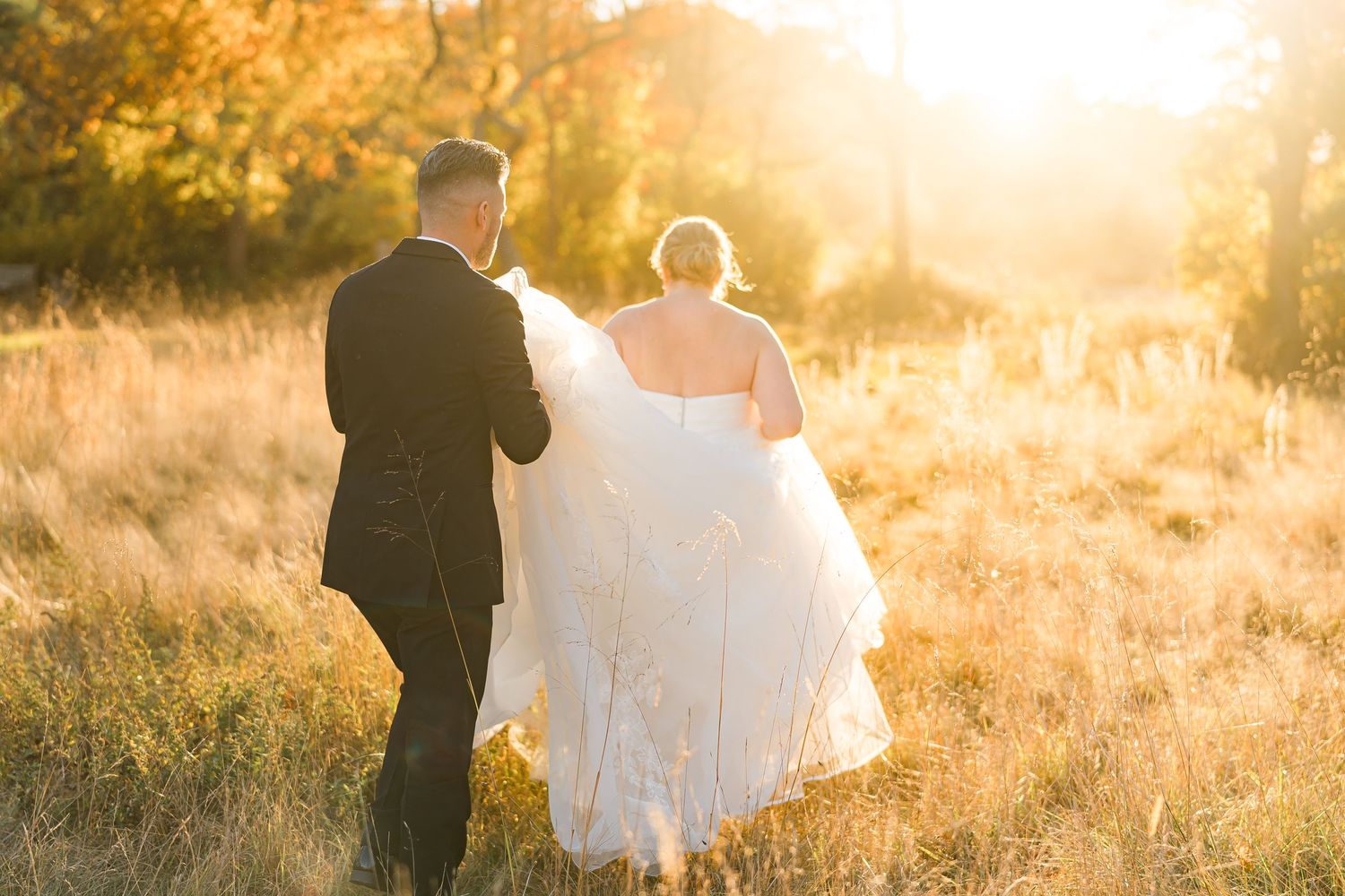 A couple walks through a sun-drenched field during golden hour on their wedding day.