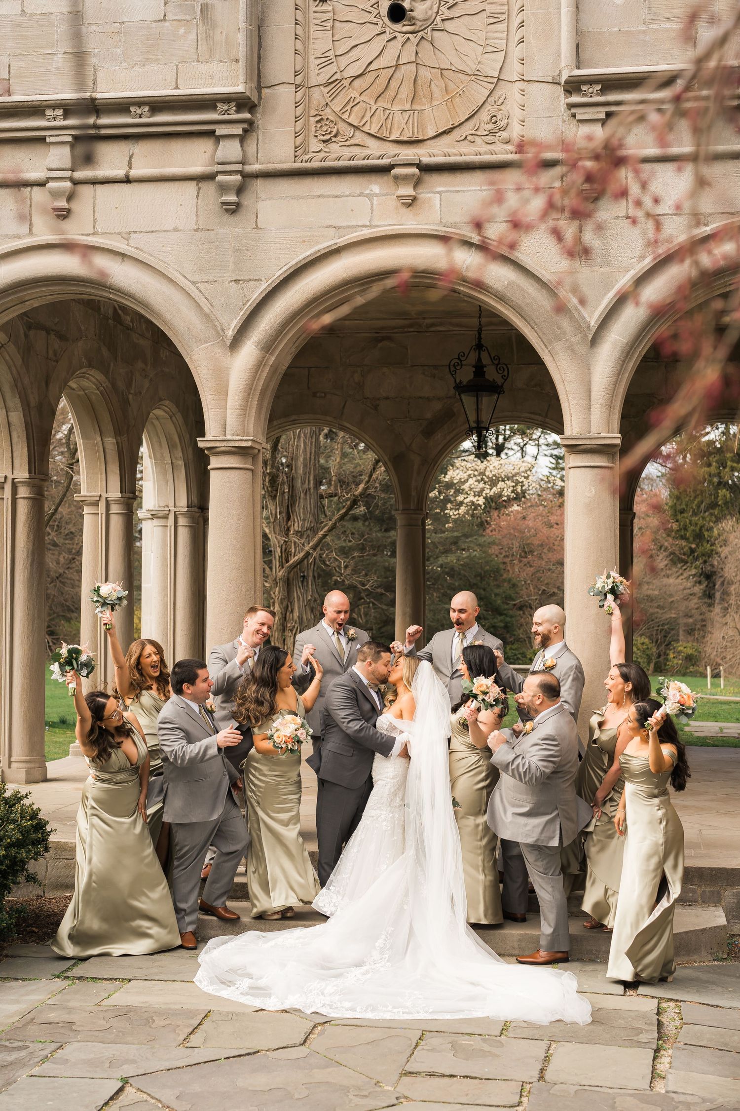 Wedding party poses together under stone archway with cathedral architecture and long white wedding train.