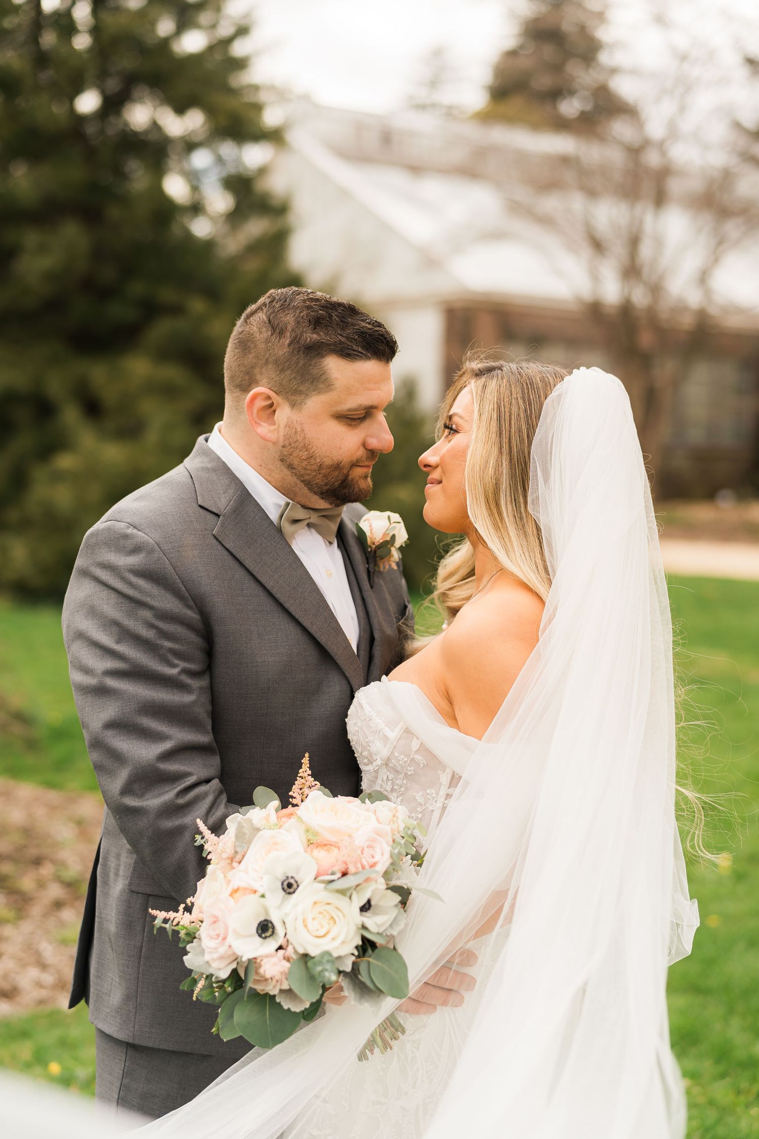 Wedding couple shares intimate moment outdoors with pink floral bouquet.