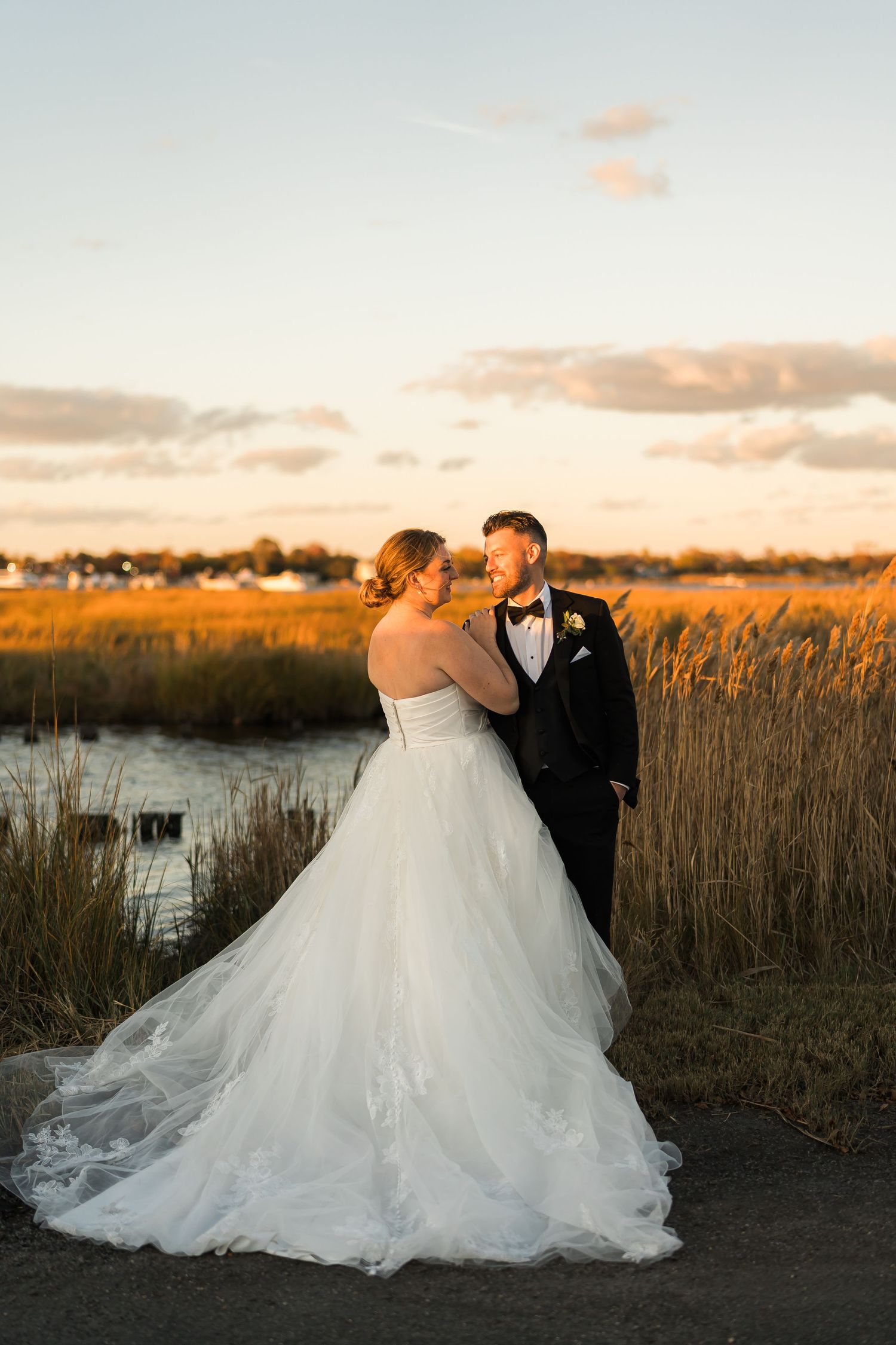 Romantic sunset portrait of newlyweds embracing near marshland with dramatic sky.