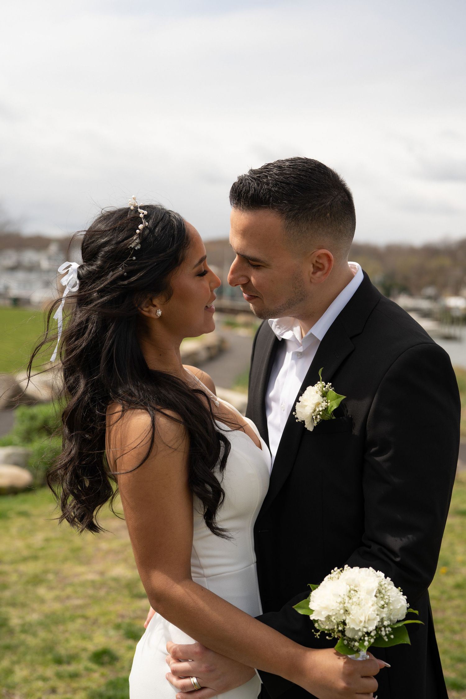 A couple shares romantic moments on their wedding day in an outdoor setting with white flowers and formal attire.