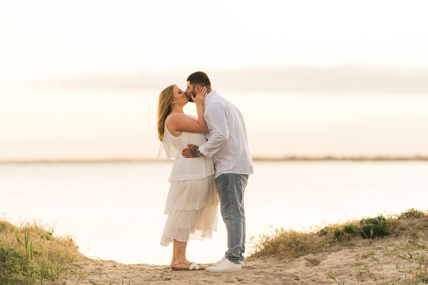 A romantic couple shares an intimate moment at sunset on a sandy beach overlook.