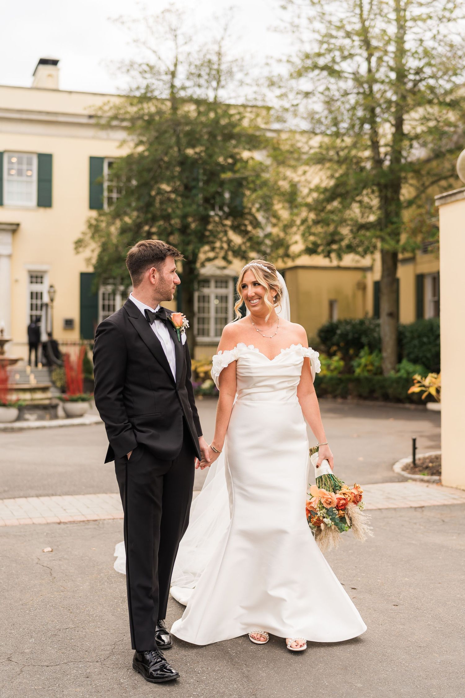 Elegant wedding couple poses together outside a stately cream-colored building with green shutters.