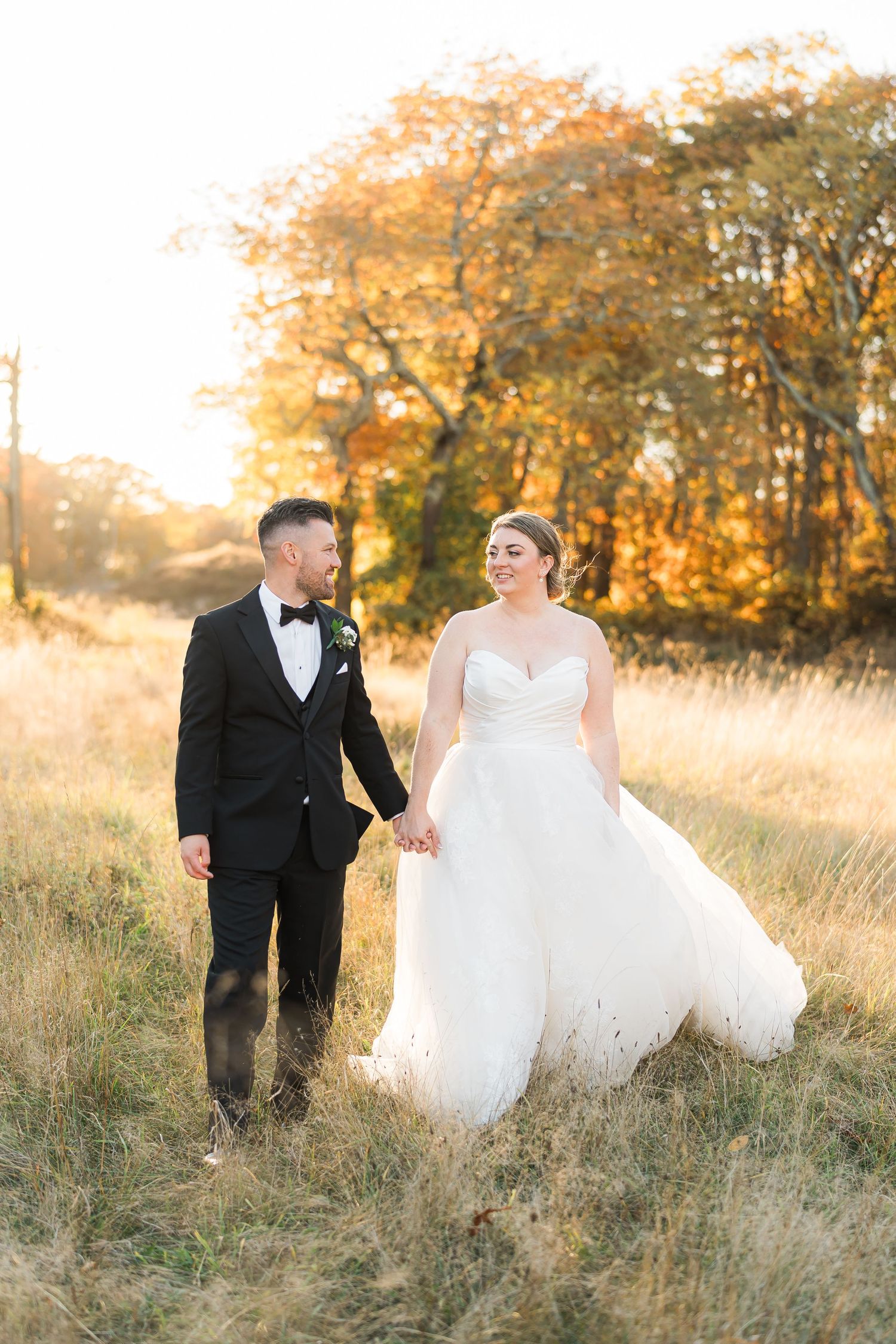A wedding couple walks through a golden autumn field at sunset.